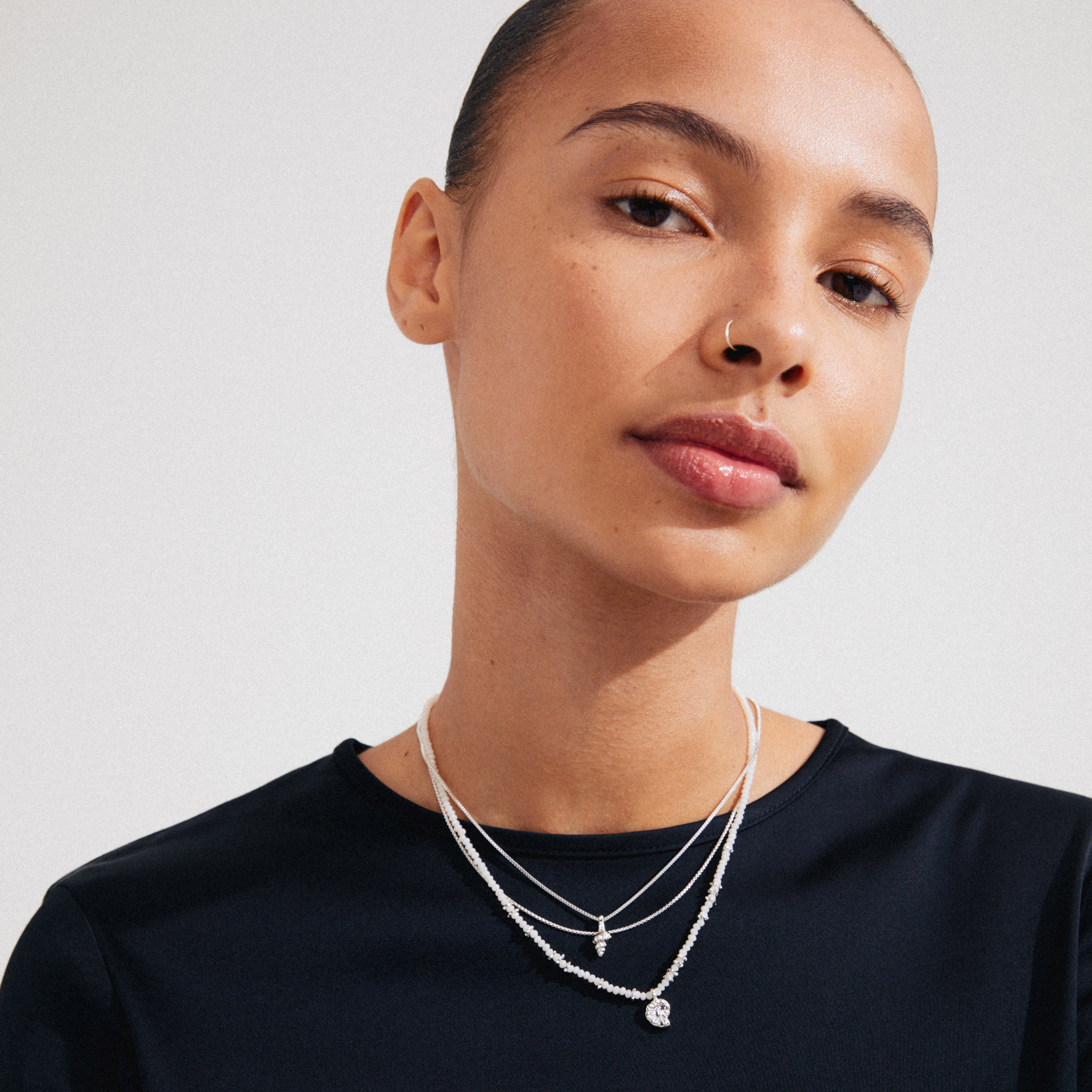 Woman wearing SEA necklace, 3-in-1 set with three delicate silver-plated chains featuring ammonite and conch pendants, showcasing a bohemian style.