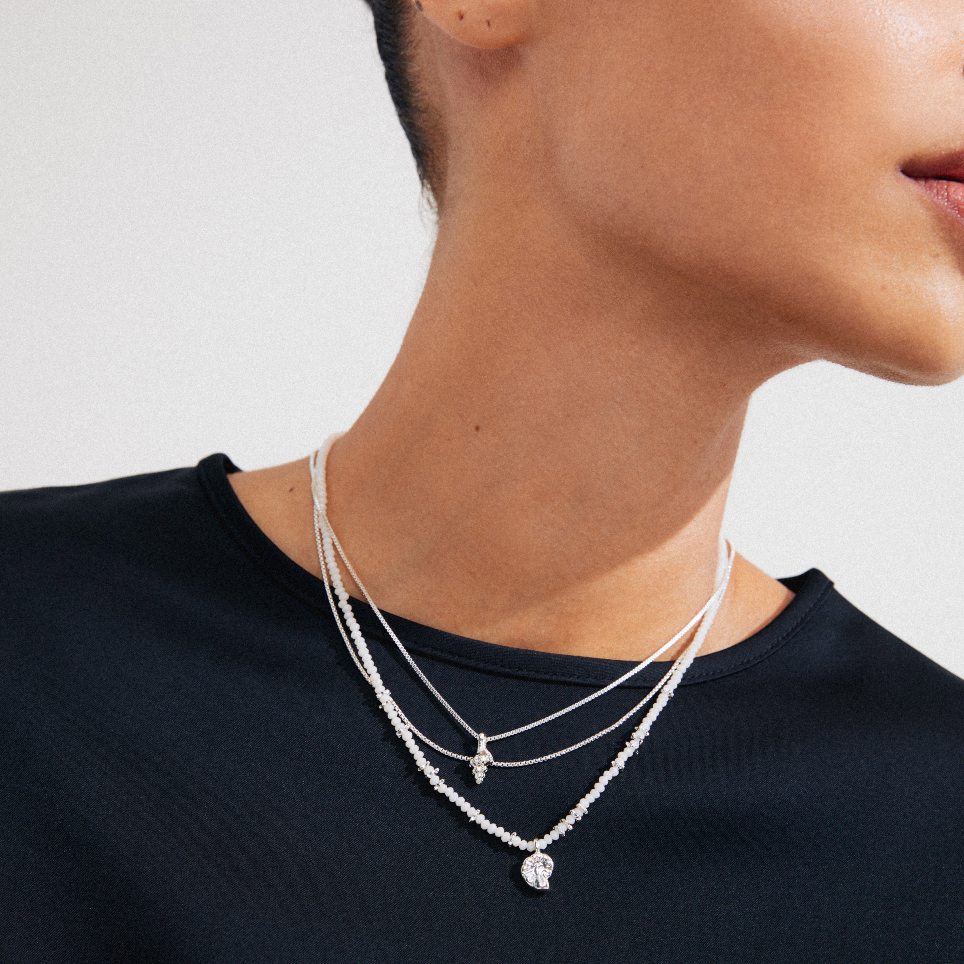 Woman wearing SEA necklace set: three silver-plated chains with ammonite and conch pendants, part of Pilgrim's Shapes Of Life collection.