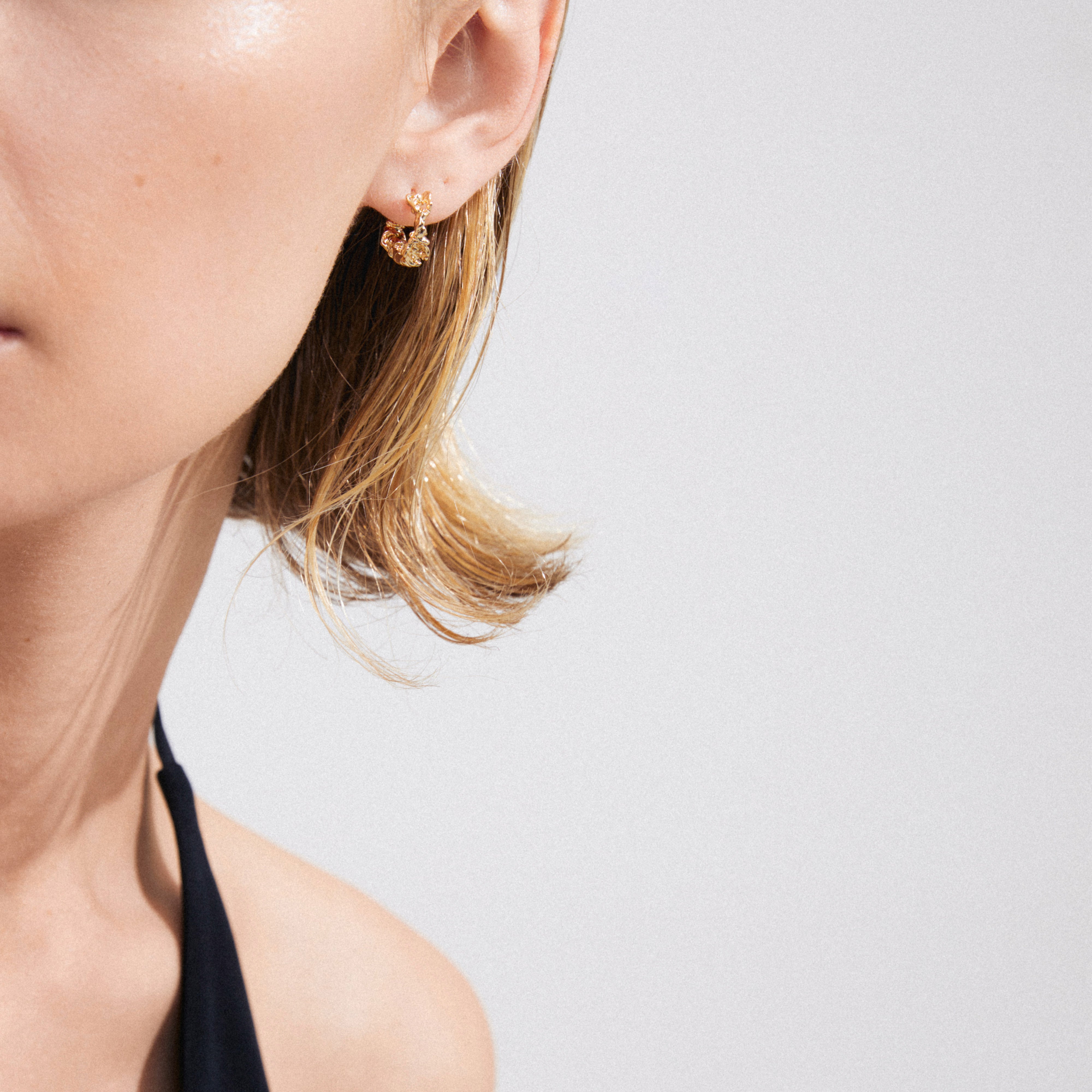 Close-up of a person wearing Pilgrim's TRUST gold-plated hoop earrings, showcasing the rustic, handcrafted design on their earlobe.