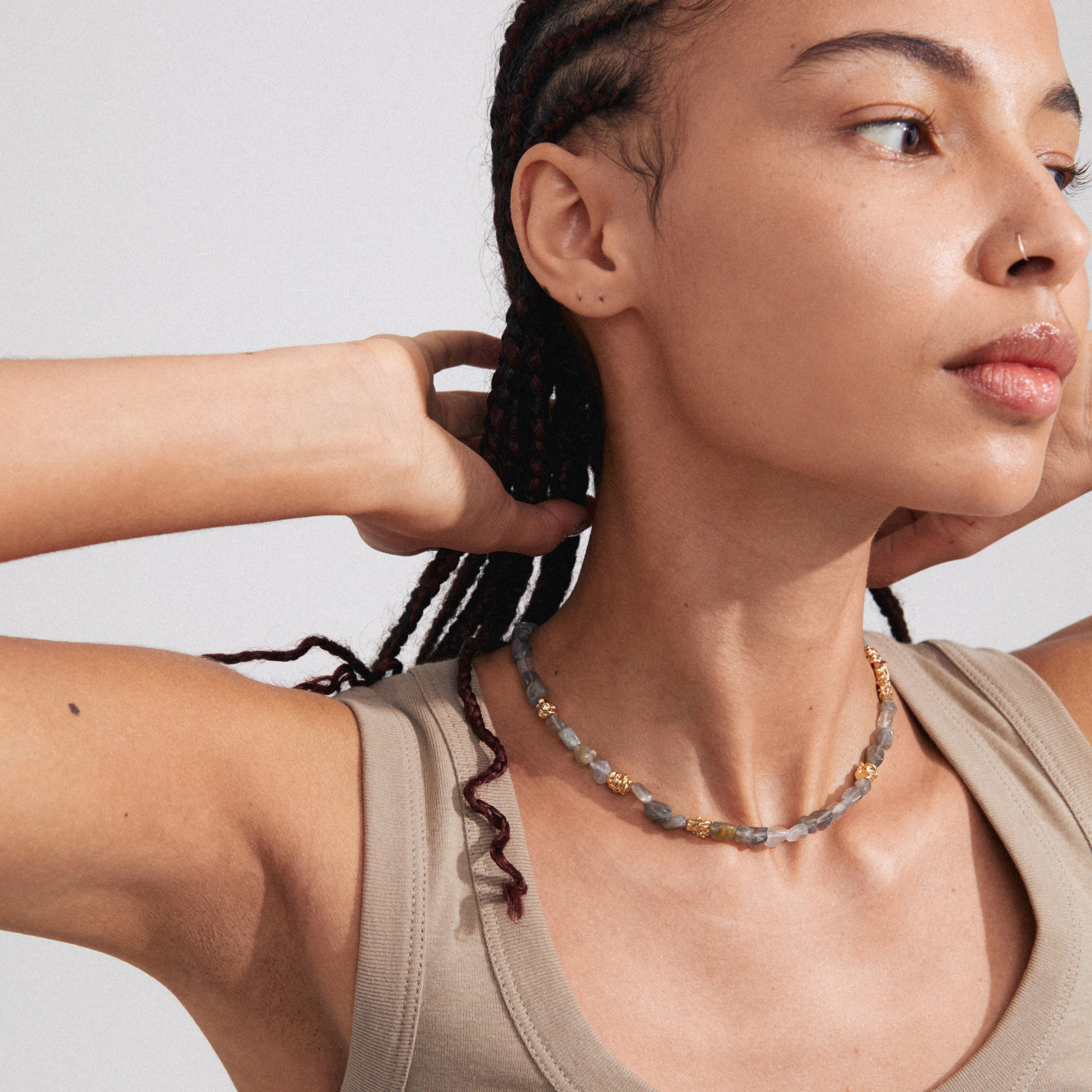 Woman modeling Pilgrim's TRUST necklace, featuring a semi-precious grey Labradorite stone, gold-plated details, and a decorative T-bar clasp, worn close to the neck.