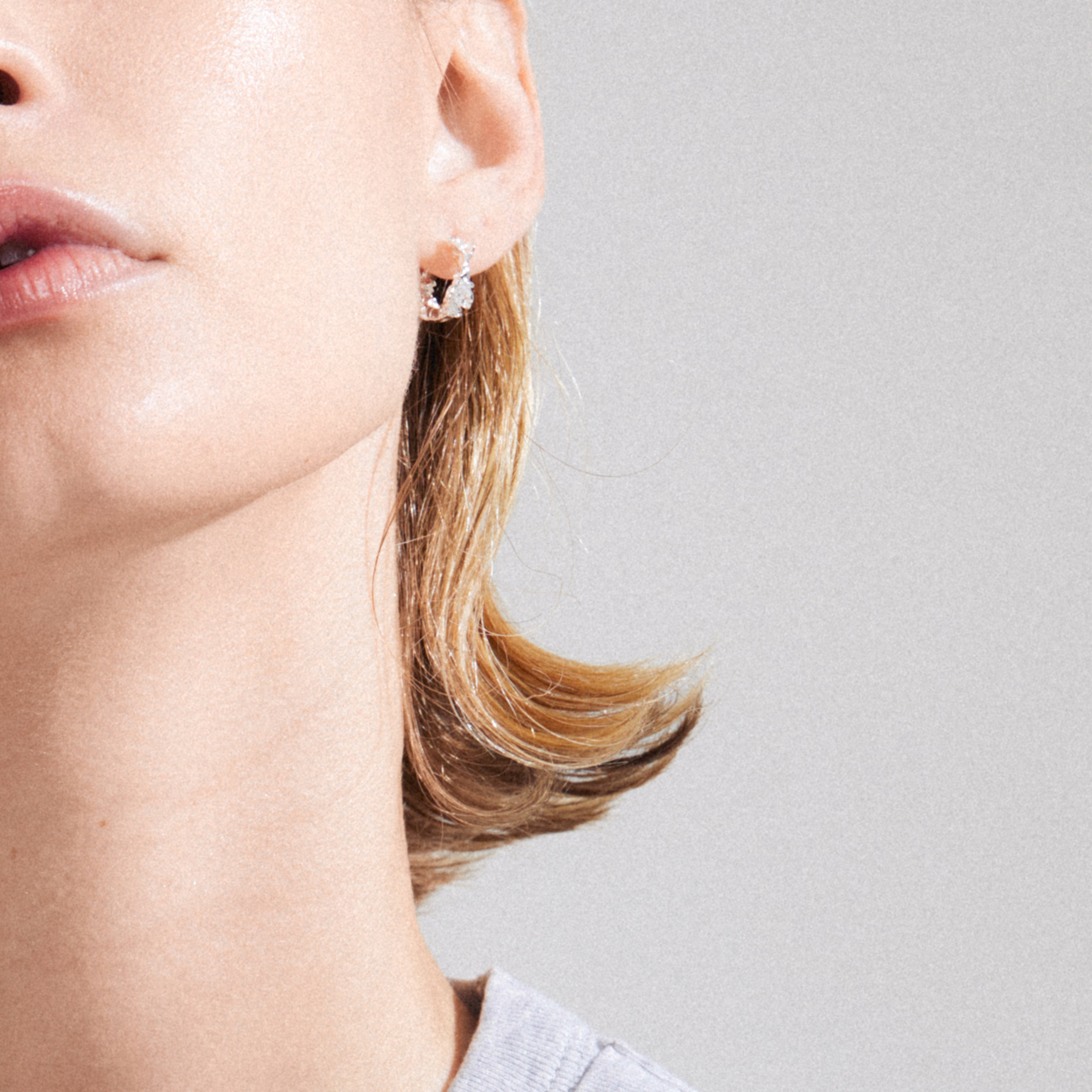 TRUST hoop earrings, silver-plated, dangling from a light-skinned person’s ear, showcasing a simple, rustic design handcrafted from 99% recycled material.