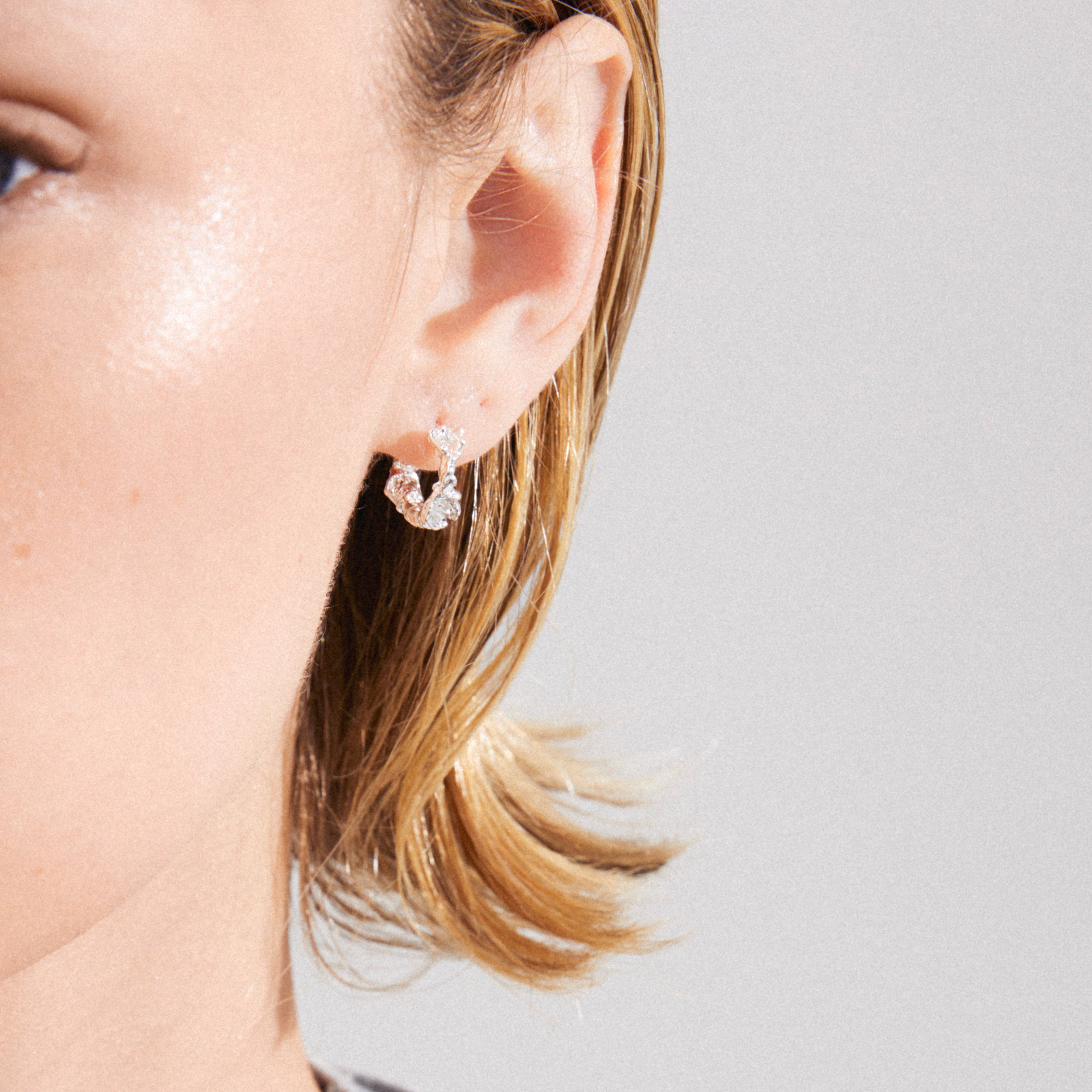 Close-up of TRUST hoop earrings, silver-plated with clear stones, worn on an ear. Features an easy click clasp, embodying a handcrafted, authentic vibe.