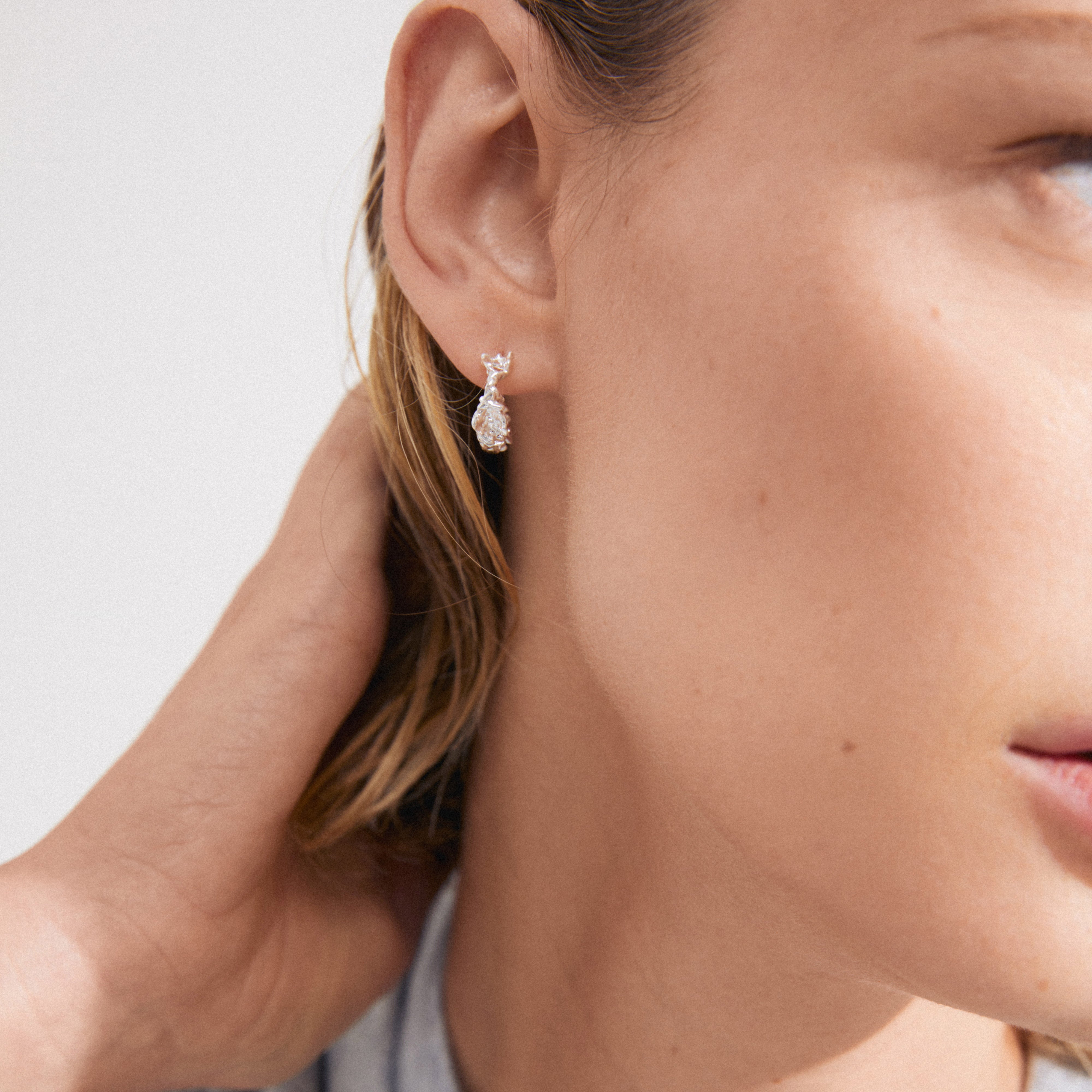 Close-up of a woman's ear wearing TRUST silver-plated huggie hoop earrings, showcasing a simple, rustic design with an organic, handcrafted feel.