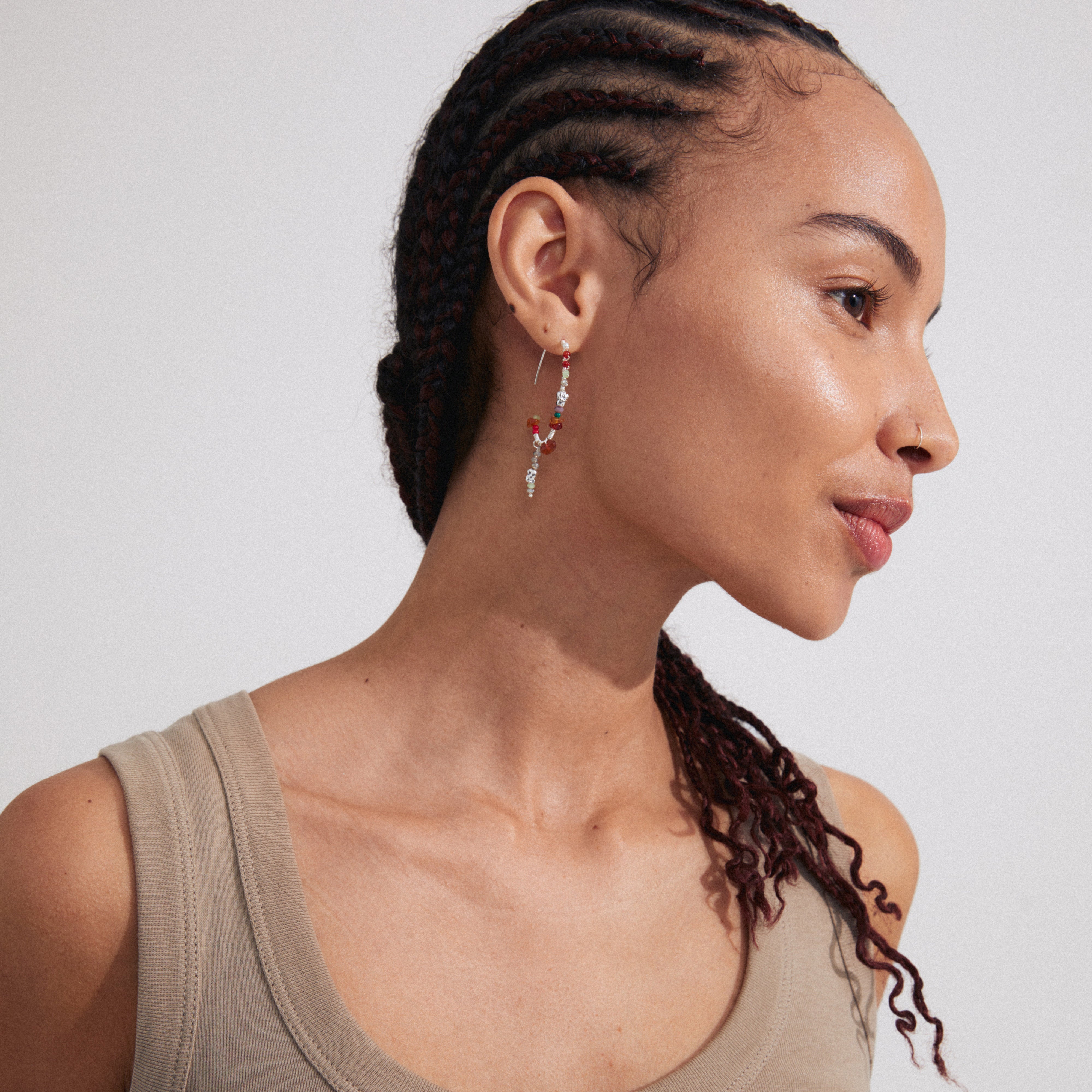 Woman wearing TRUST half hoop earrings, silver-plated, with a handcrafted vibe, featuring semi-precious stones. Highlights Pilgrim's luxurious bohemian style. Close-up on earrings and braided hairstyle.