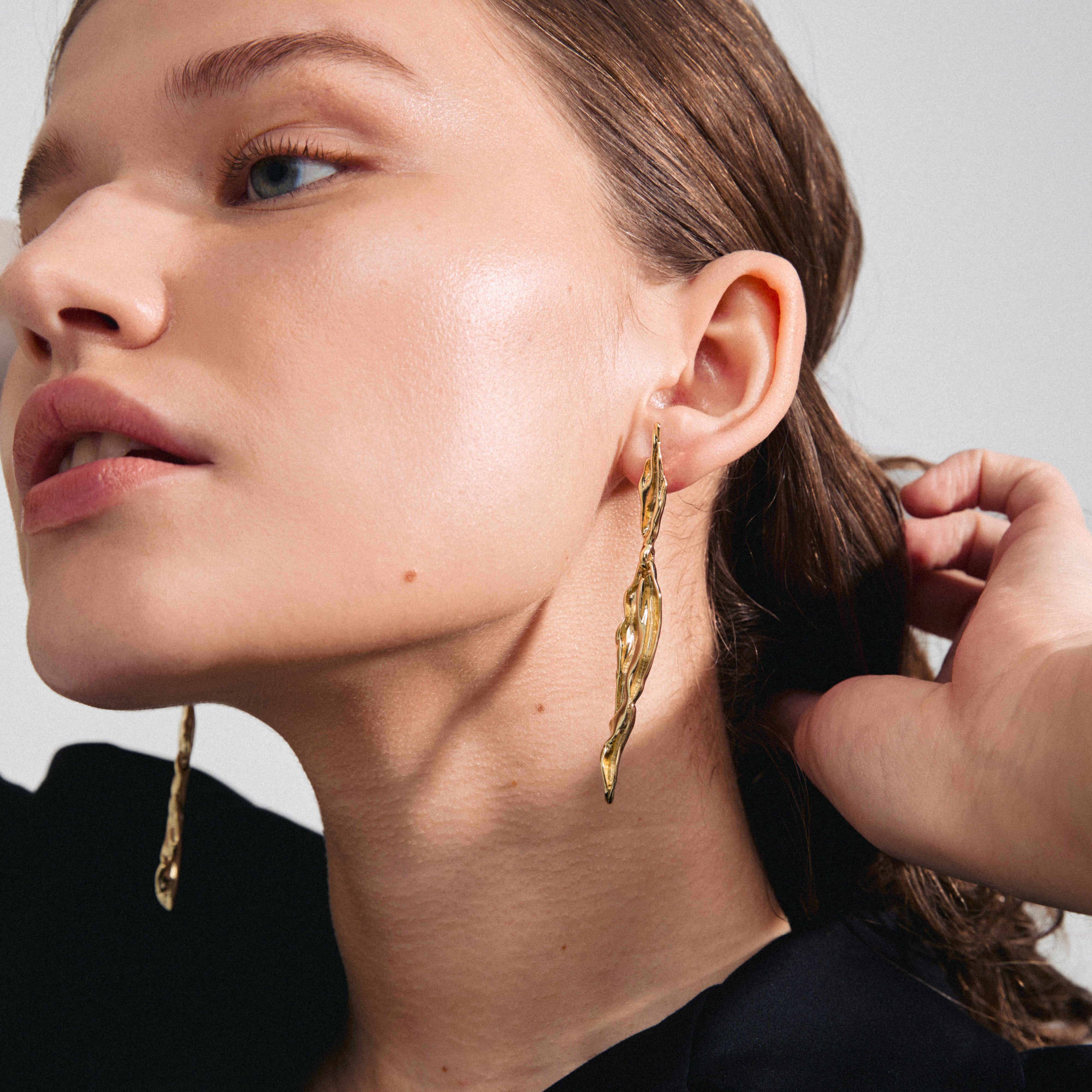 FEEL earrings gold-plated with wavy, organic design, worn by a woman, showcasing Pilgrim's blend of classic and stylish fashion accessories. Made from 97% recycled material.