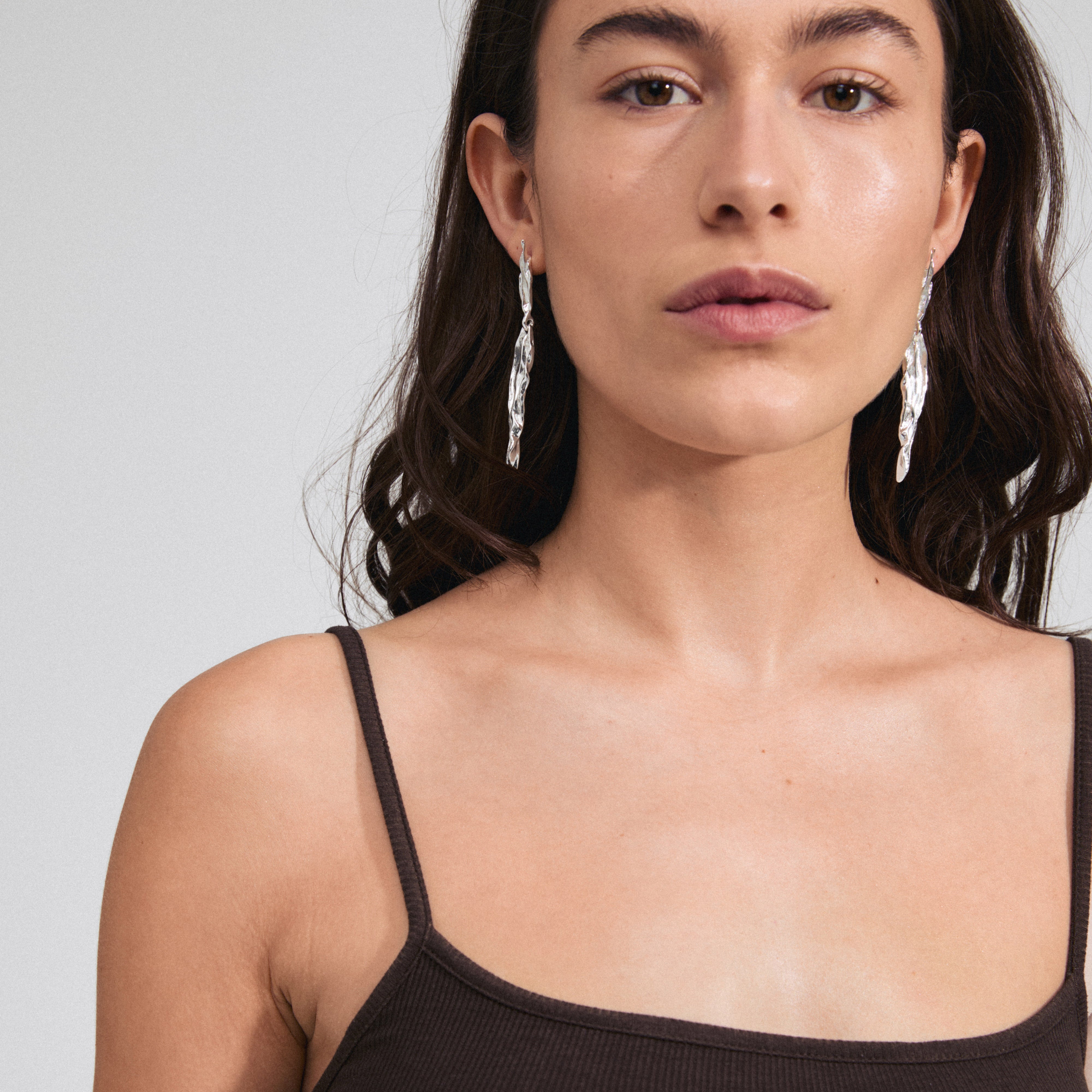 Woman with long hair wearing Pilgrim's FEEL silver-plated earrings, showcasing their sleek, fluid design inspired by nature's silhouettes.