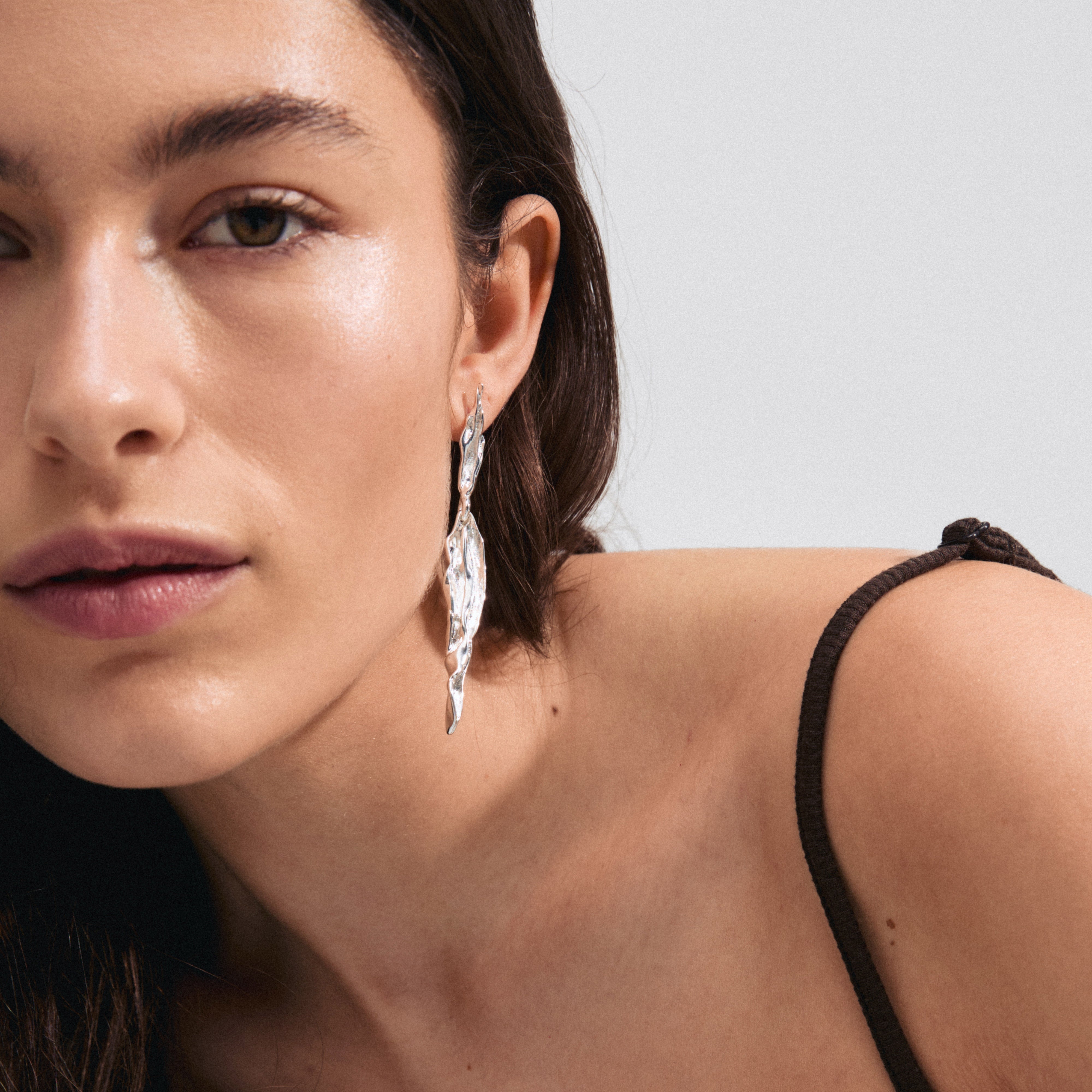 FEEL earrings silver-plated with sleek, wavy design, inspired by nature. Showcased on a woman, highlighting their fluid style and recycled material craftsmanship.