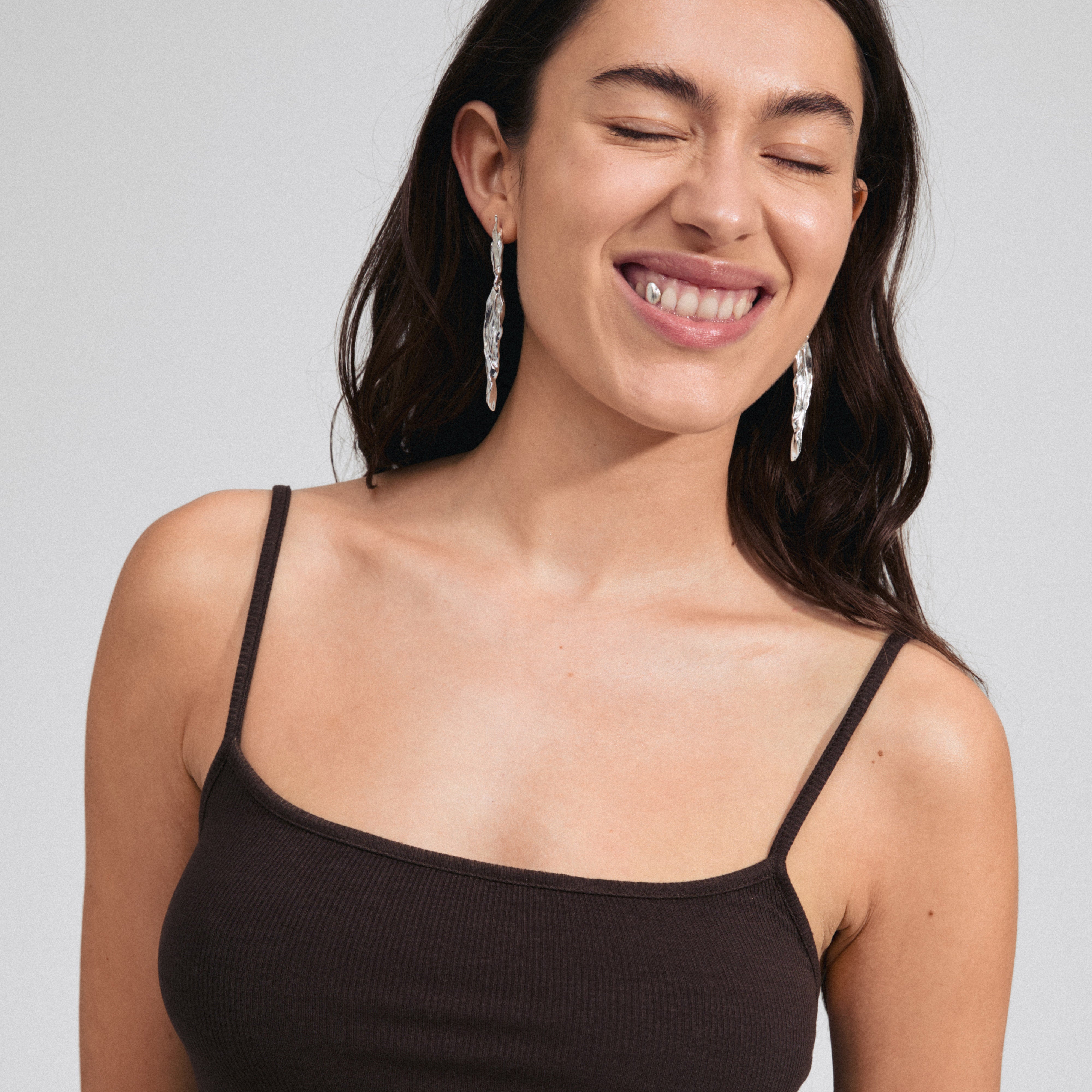 Silver-plated FEEL earrings featuring a sleek, wavy design, worn by a smiling woman with closed eyes, showcasing their stylish and organic elegance.