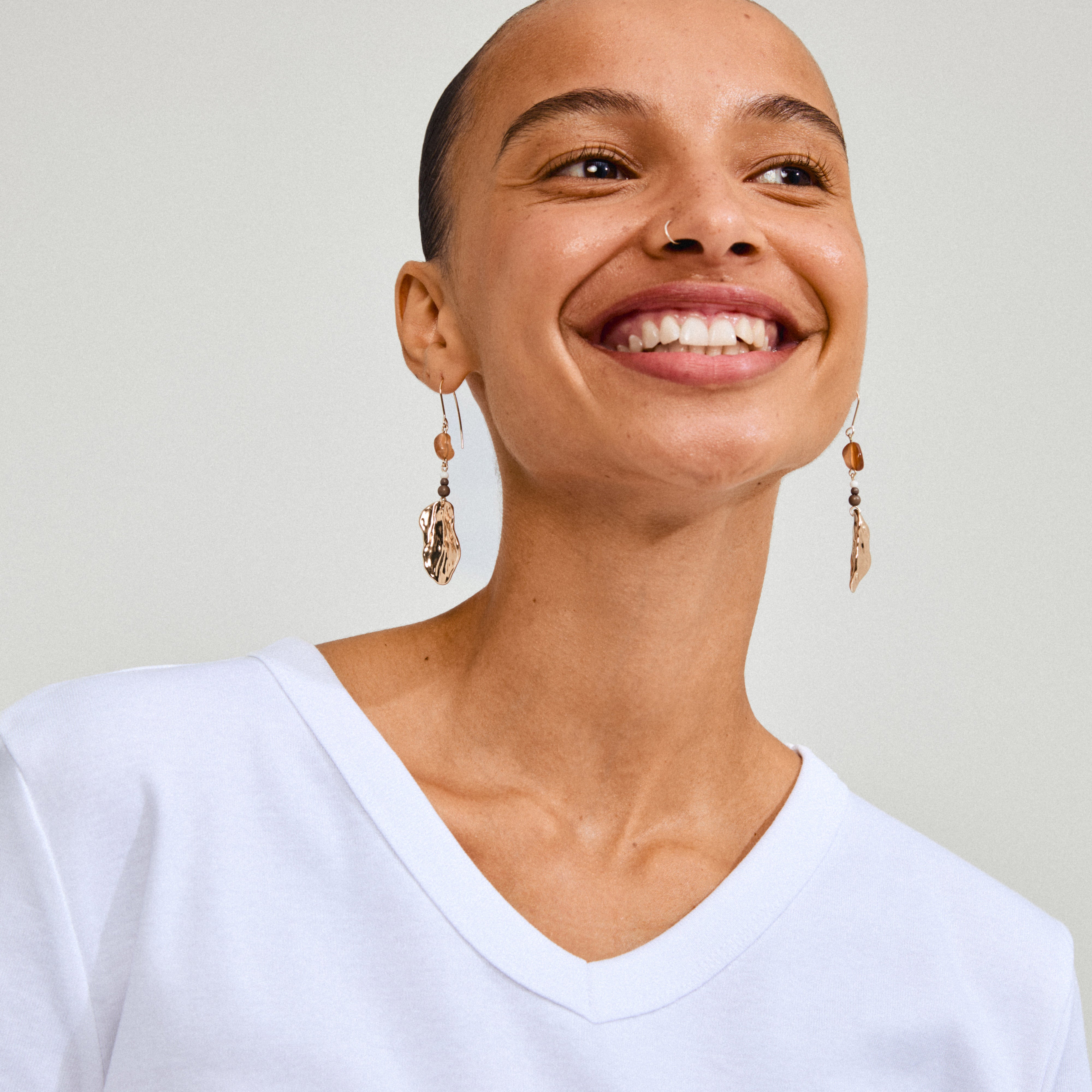 Gold-plated ECLIPSE earrings featuring organic pendants and red Agate, worn by a smiling woman, capturing light with a wavy surface.