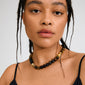 Model wearing the UNFOLD necklace gold-plated/brown with alternating Tiger Eye beads in black, brown, and honey-yellow, featuring a decorative gold-plated clasp.
