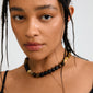 Young person wearing the UNFOLD necklace by Pilgrim, featuring black and brownish-gold Tiger Eye beads with a gold-plated clasp, highlighting its trendy and protective qualities.