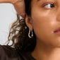 Close-up of a person's ear wearing the silver-plated UNFOLD hoops by Pilgrim, featuring a free-form design and shiny finish, complementing dark curly hair.