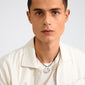 Young man wearing the UNFOLD necklace, a silver-plated piece with interlocking rings on a black cord, complementing his casual cream shirt and white T-shirt.