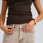 Person wearing a dark brown top and sandy-wash jeans, showcasing the UNFOLD bracelet with earth-toned beads and silver-plated pendants from Pilgrim.