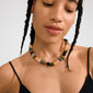 A person wears the UNFOLD necklace by Pilgrim, featuring multicolored round beads and a silver-plated clasp, styled with a sleeveless black top and braided hair.