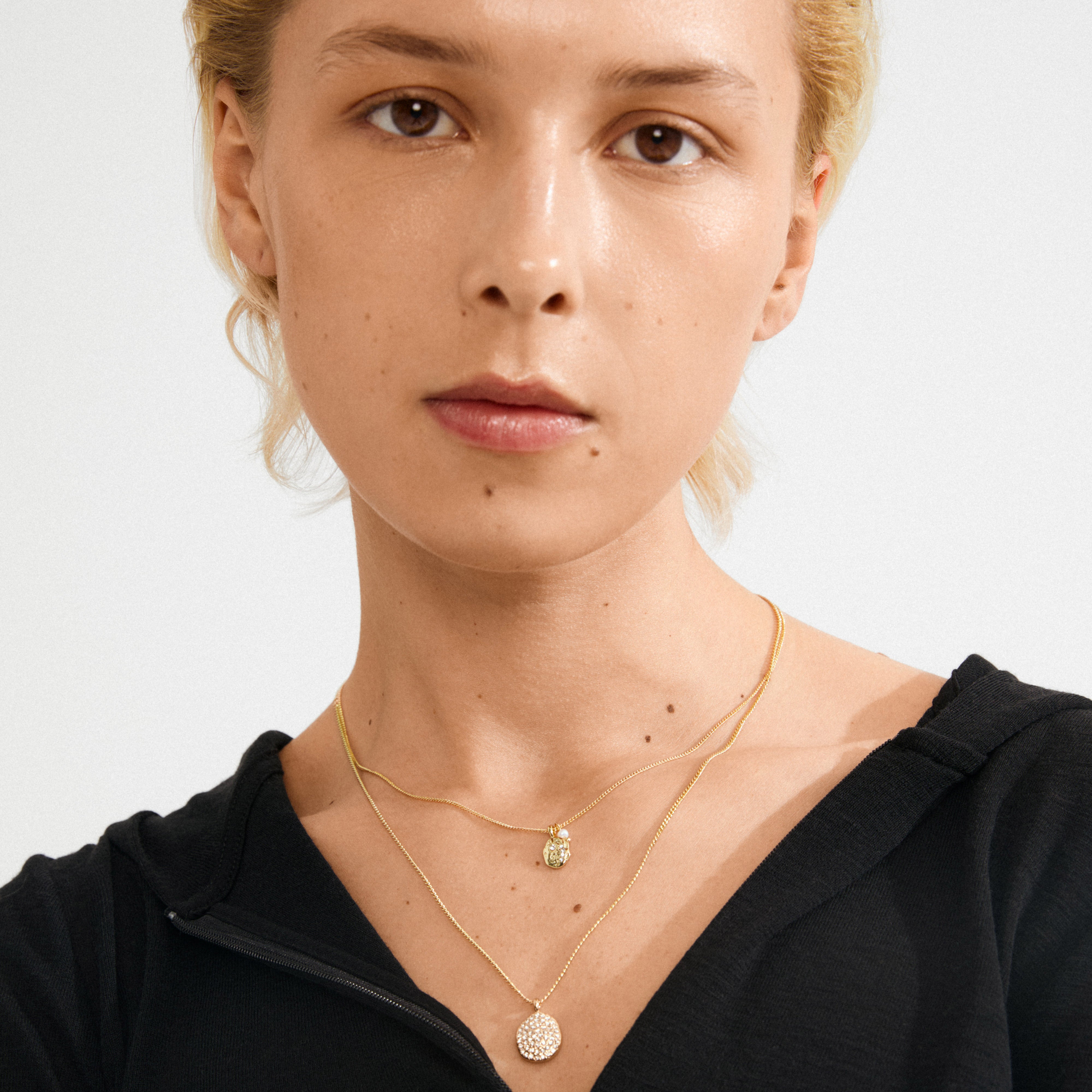 Close-up of a person wearing Pilgrim's SHIFT necklace 2-in-1 set, gold-plated, featuring two layered chains with crystal-studded pendants.