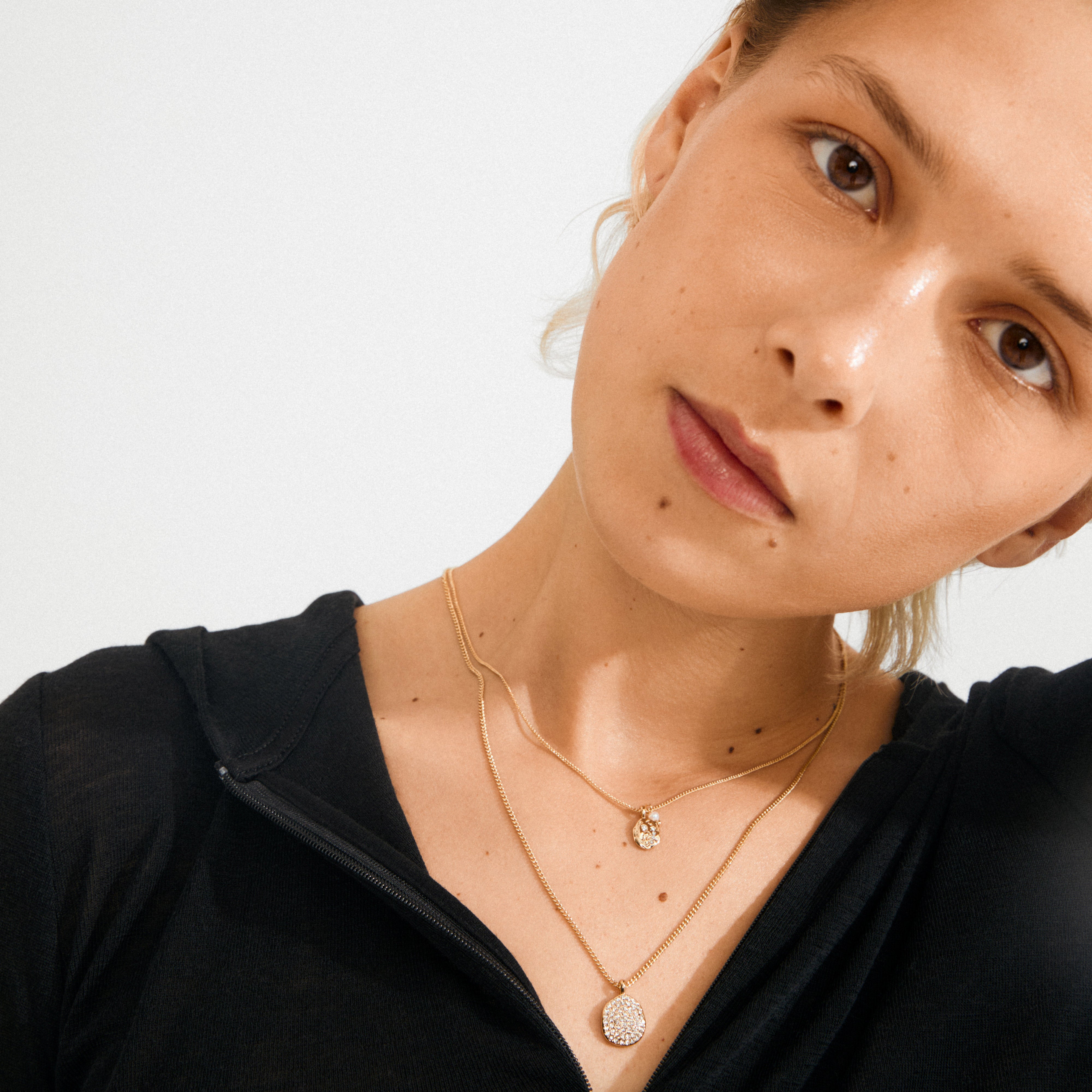 Young adult wearing Pilgrim's SHIFT necklace 2-in-1 set, featuring gold-plated layers with crystal-studded pendants and a pearl, showcasing a chic, layered style.