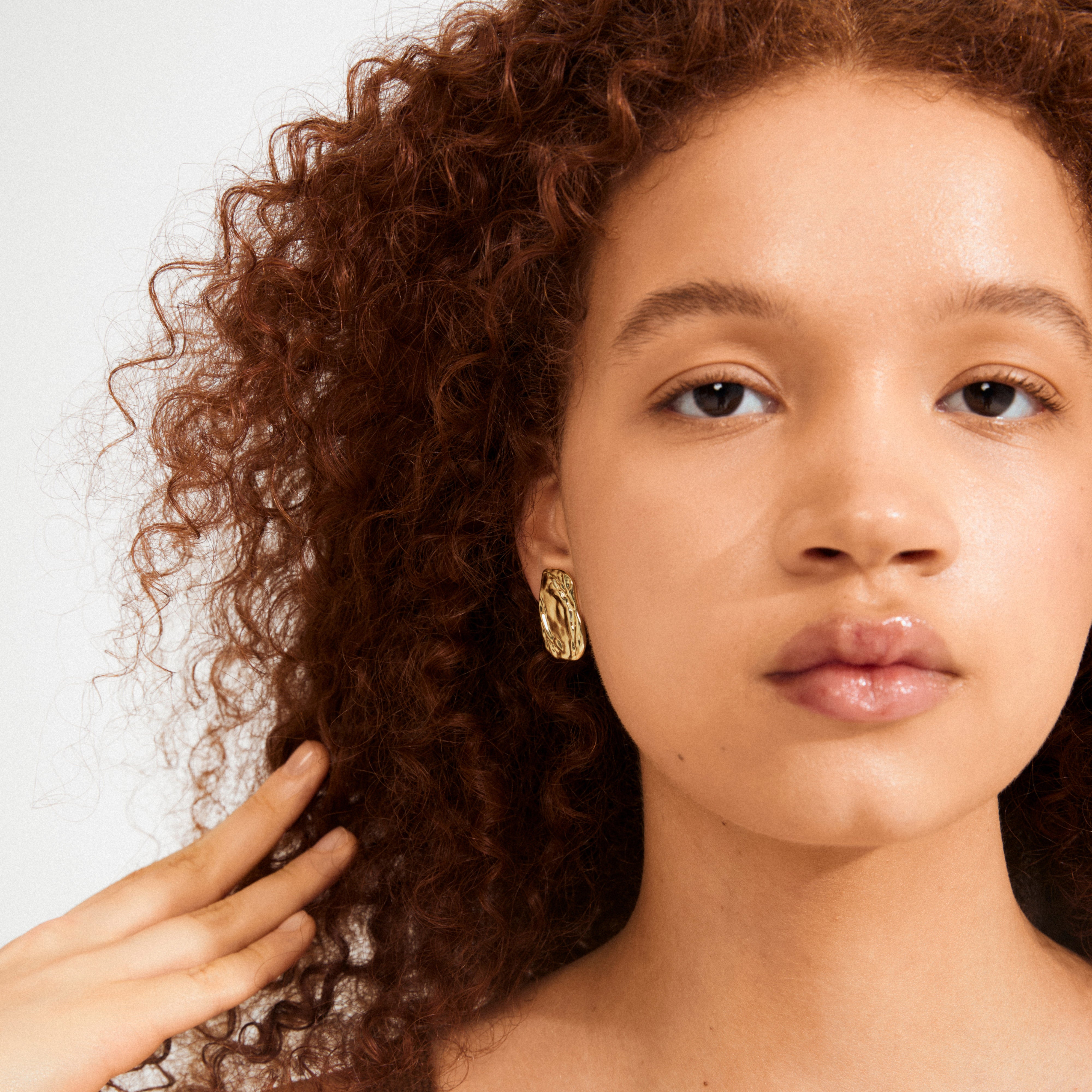 Young person wearing a sculptural gold-plated SHIFT earring by Pilgrim, showcasing a chic, handcrafted style with a focus on modern elegance.