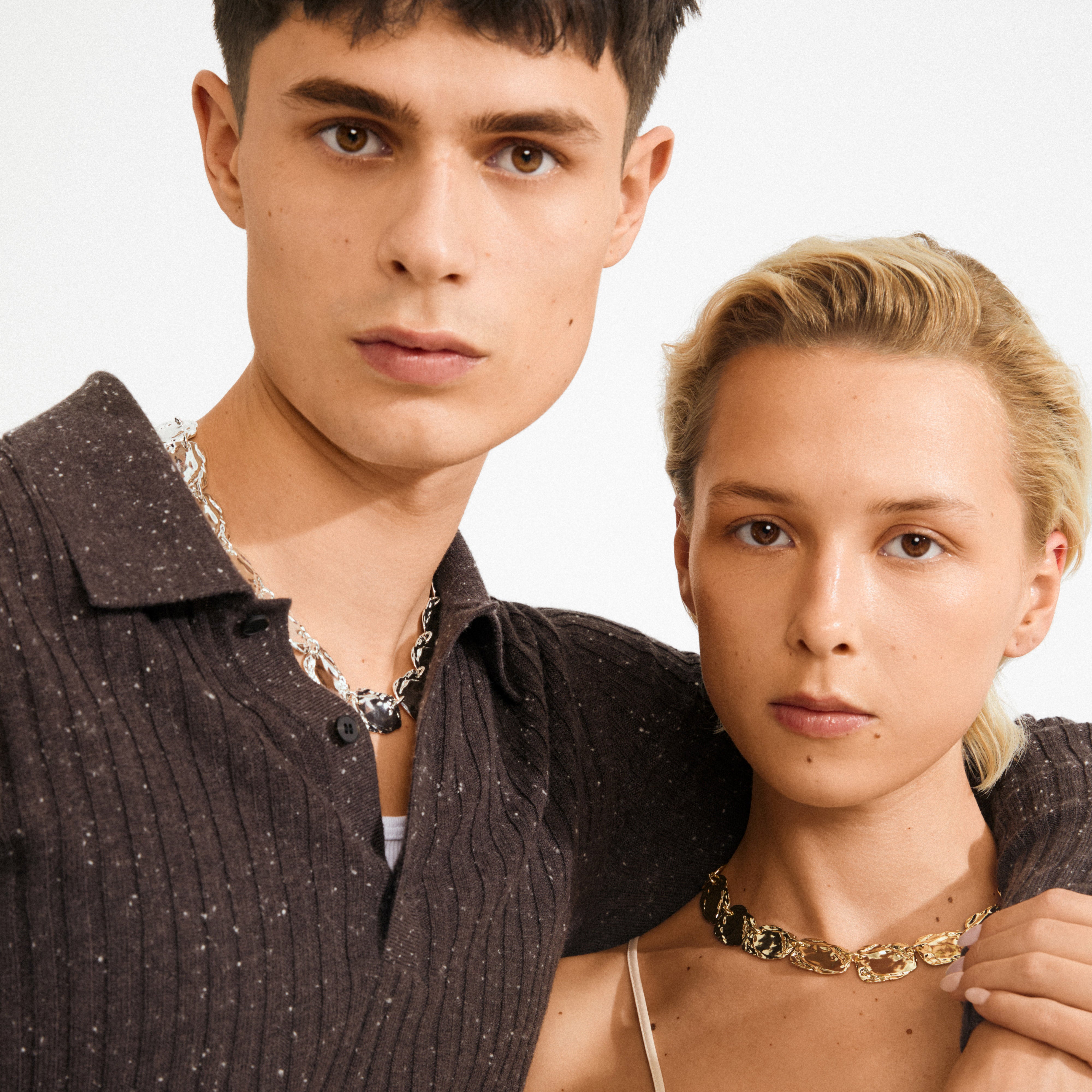 Two young adults wearing Pilgrim's SHIFT necklace; the woman sports a gold-plated chain with flat coins, embodying Scandinavian style and modern elegance.