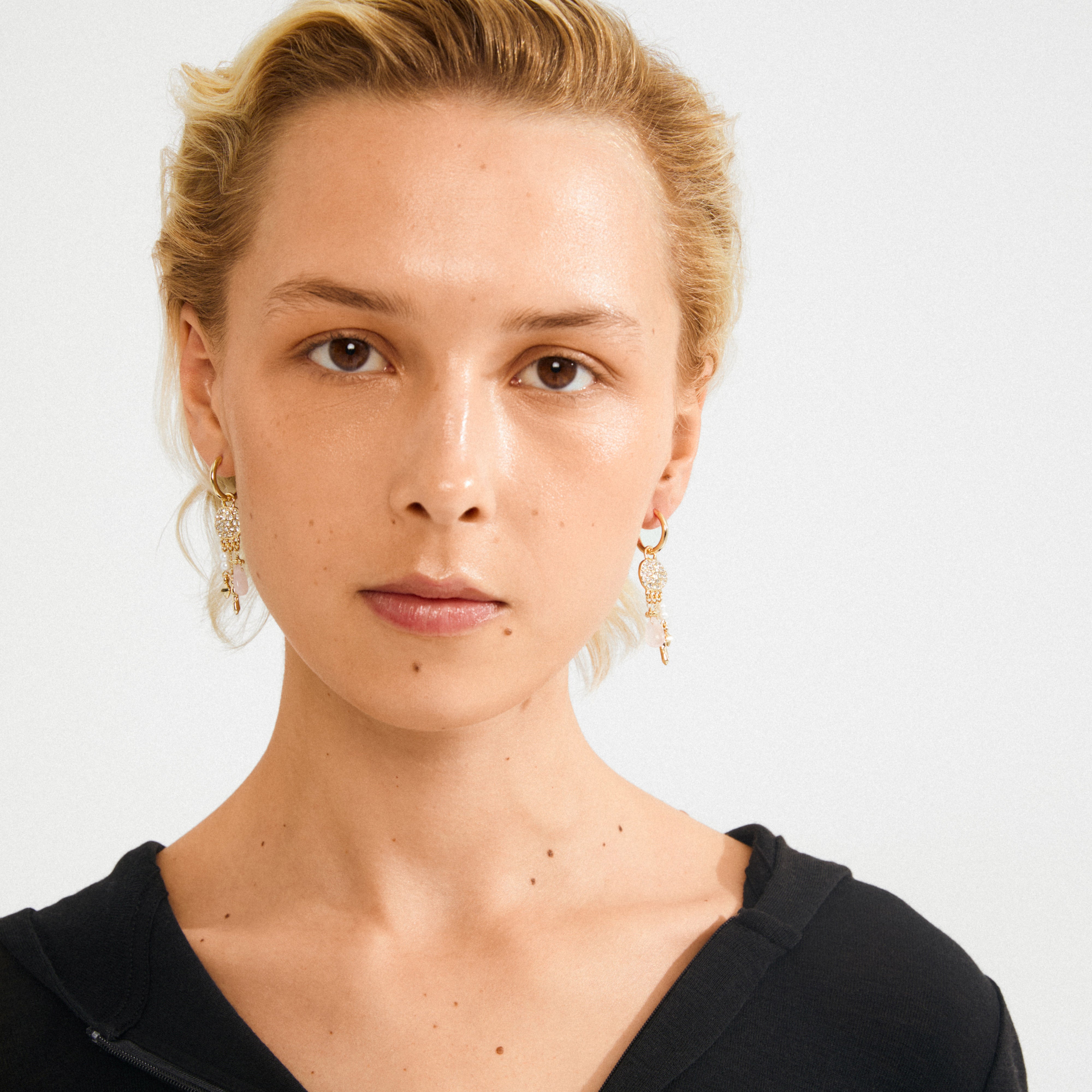 Young adult wearing SHIFT hoop earrings, gold-plated with small coin pendants, Preciosa crystals, and pearlescent glass beads, showcasing Pilgrim's boho chic elegance.