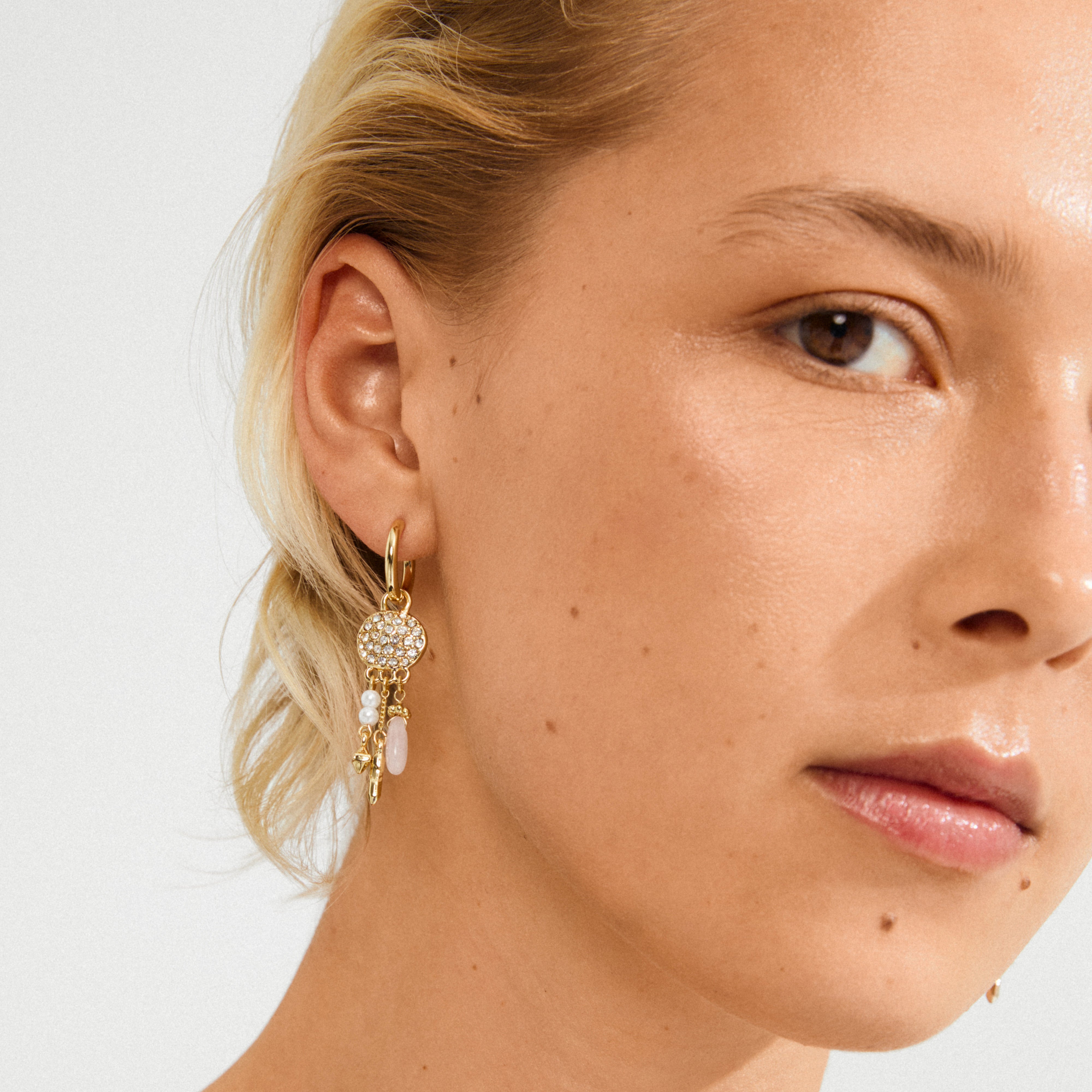 Blonde woman wearing Pilgrim's SHIFT hoop earrings, featuring a pavé-set disc, pearls, rose quartz, and charms, highlighting boho chic and whimsical elegance.