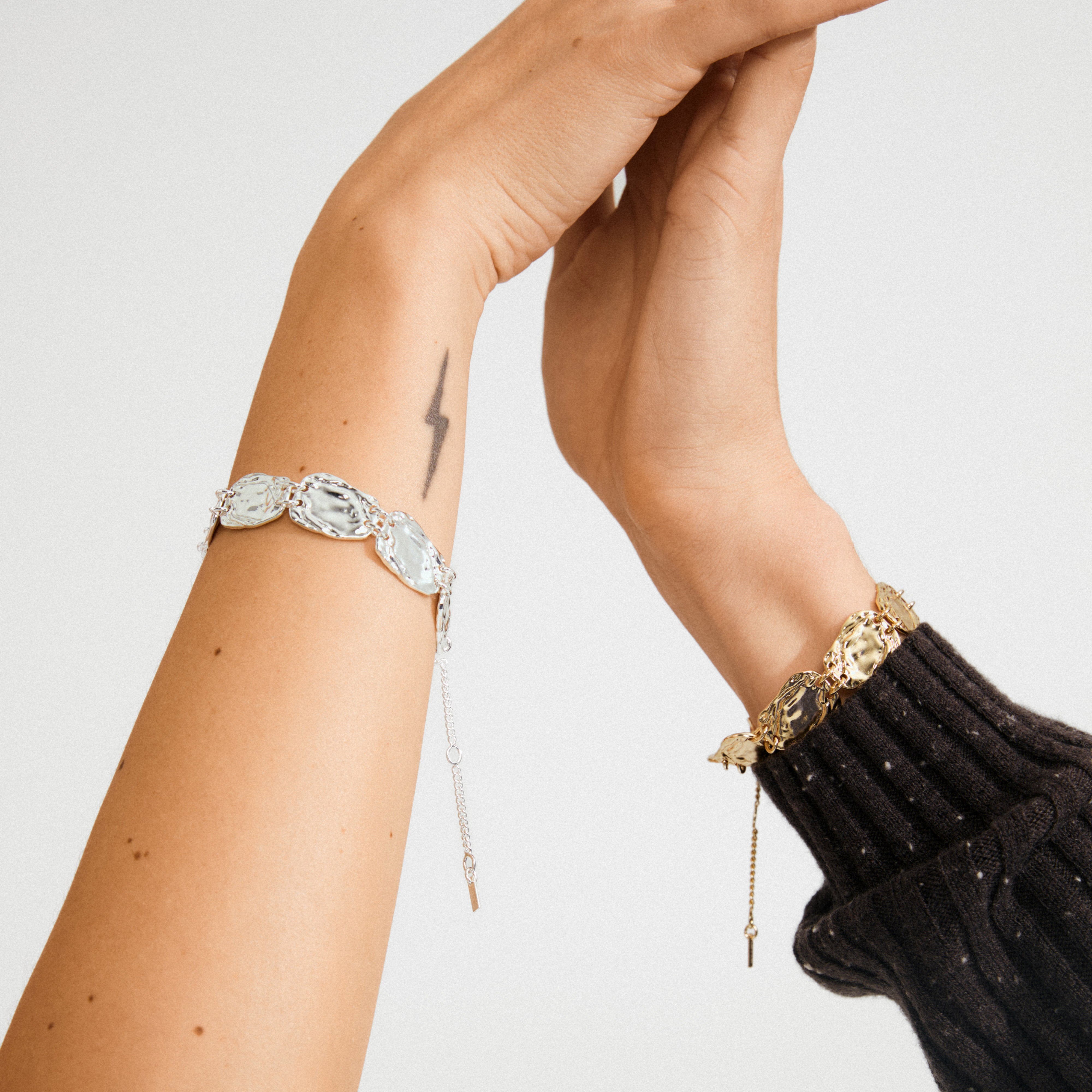 Silver-plated SHIFT bracelet on tattooed arm, featuring textured, irregular coins and chain links, embodies Pilgrim's boho-chic sophistication and Scandinavian craftsmanship.