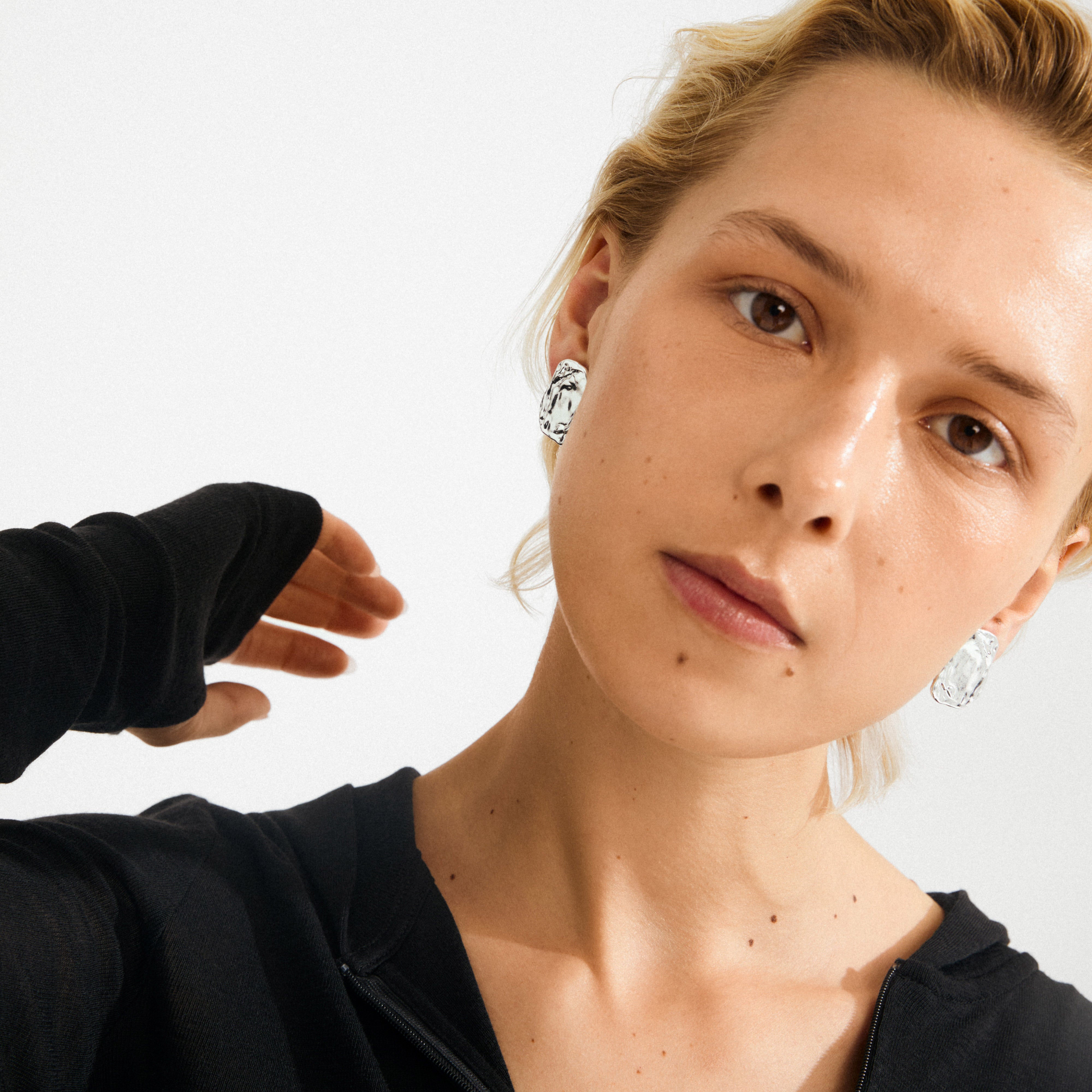 Person wearing black top and SHIFT earrings. Silver-plated, rustic design with raw finish, adding edgy elegance, reflecting Pilgrim's Scandinavian quality.