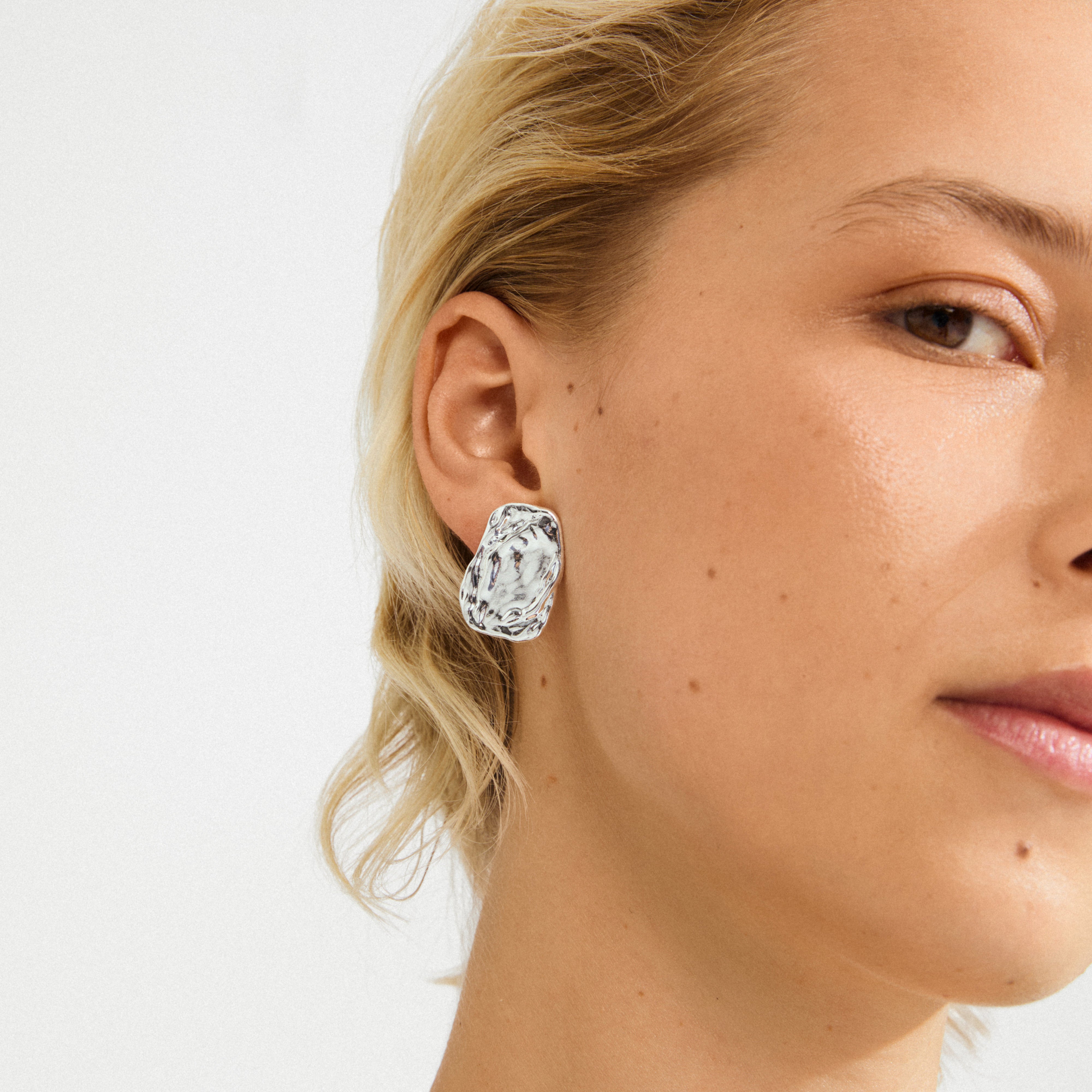 SHIFT earrings silver-plated adorn a woman's ear, featuring chunky, irregular designs with a rustic finish, embodying edgy elegance and urban coolness from Pilgrim.