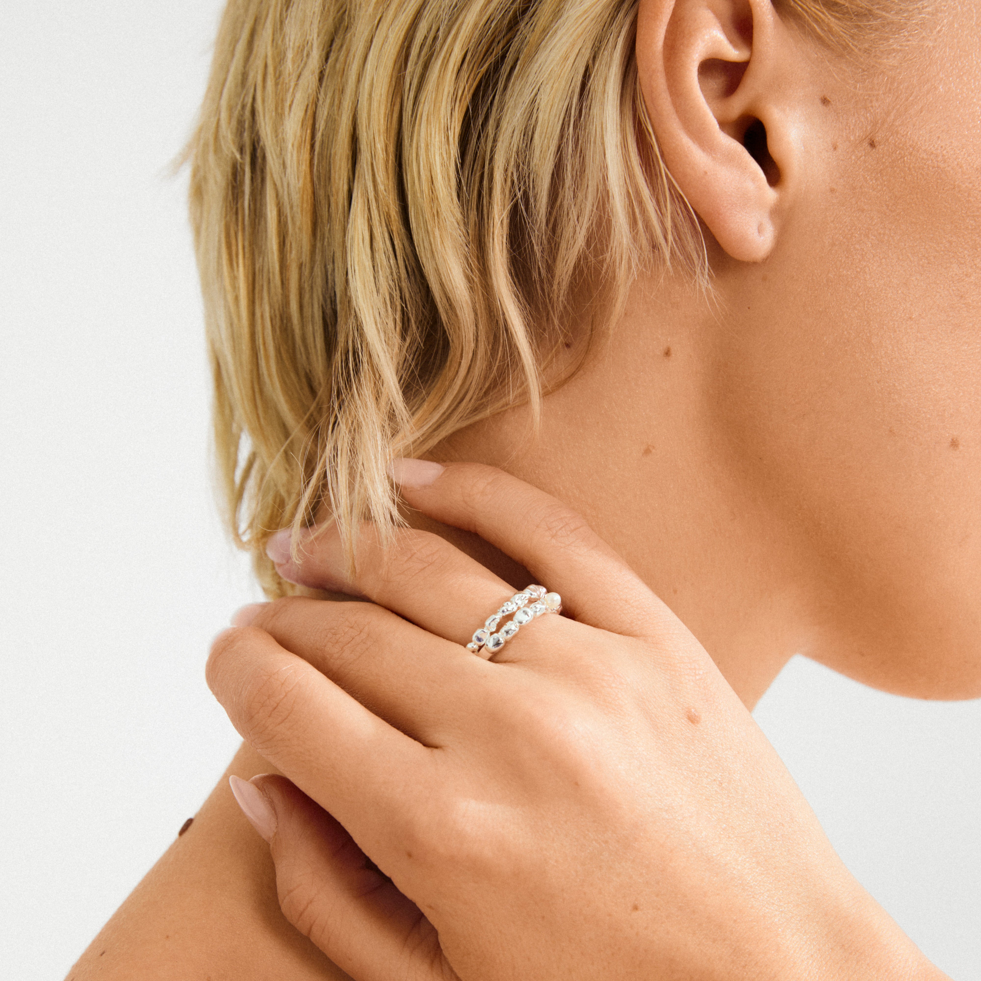 Close-up of a hand wearing the SHIFT silver-plated ring set by Pilgrim, showcasing one faceted stone ring and one beaded ring on smooth skin.
