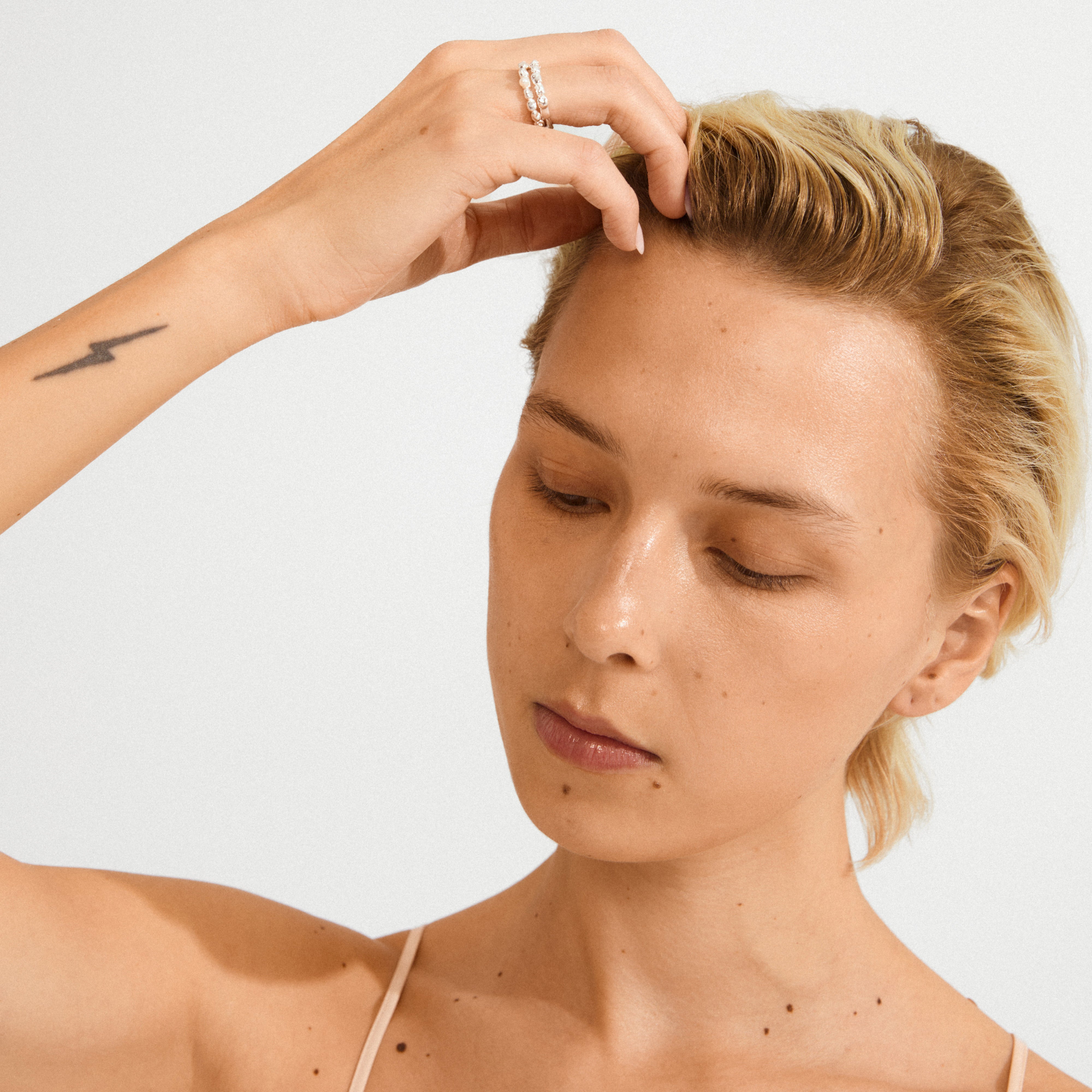 Young person with light blond hair, wearing a thin-strap top, showcases Pilgrim’s silver-plated SHIFT ring set, highlighting its organic design and pearl accent.