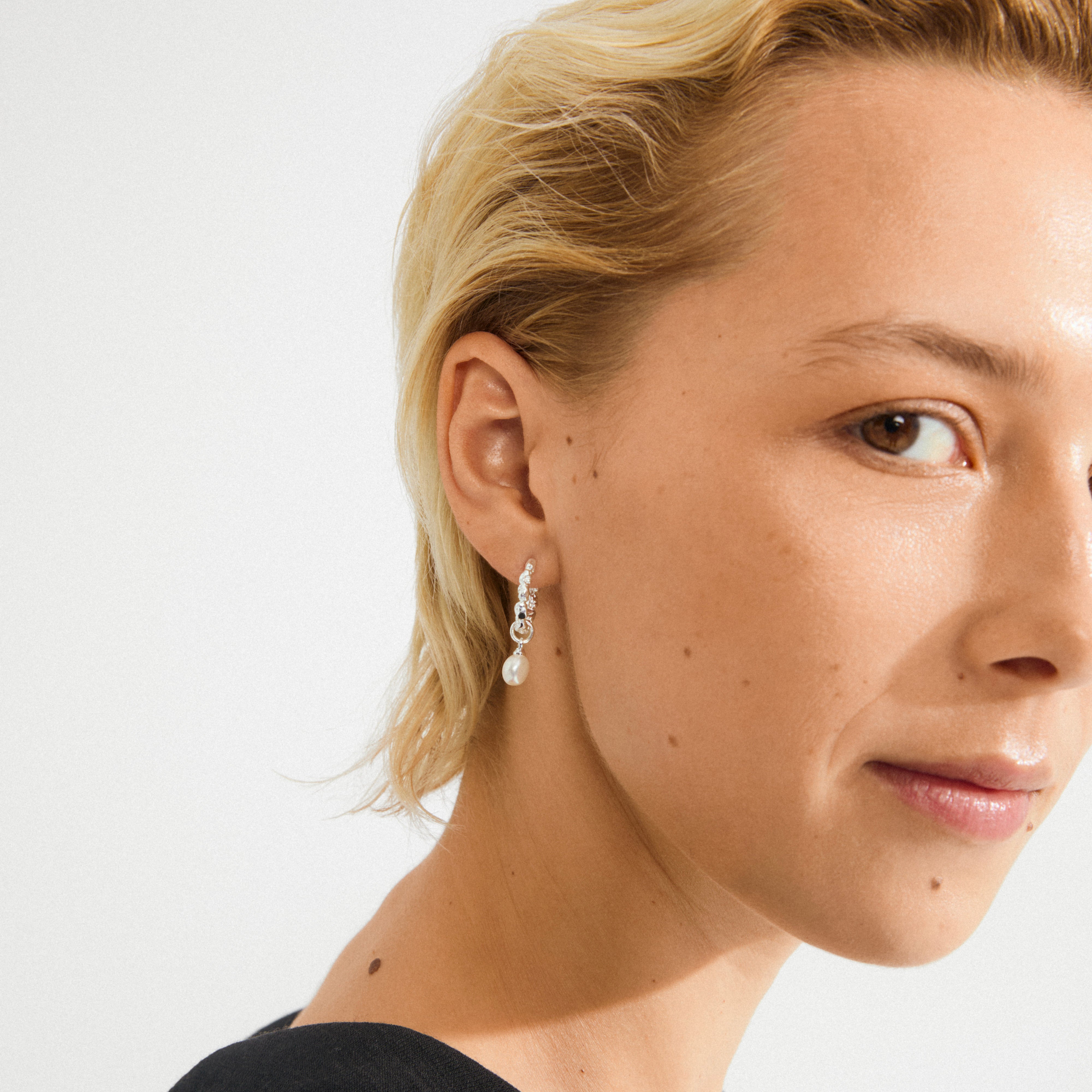 Close-up of a face wearing the SHIFT pearl earrings, silver-plated hoops with a dangling freshwater pearl, showcasing Pilgrim's blend of timeless and trendy jewellery.