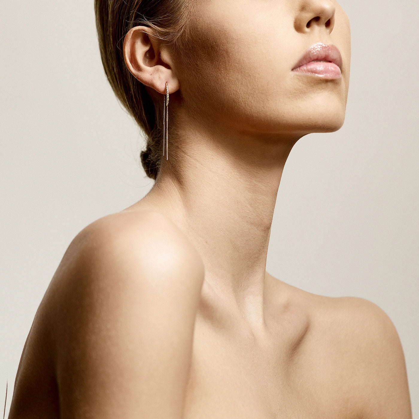 FIRE crystal earrings, gold-plated, featuring long, thin chains with clear crystals, elegantly draped from a woman's ear, showcasing a light, feminine style.