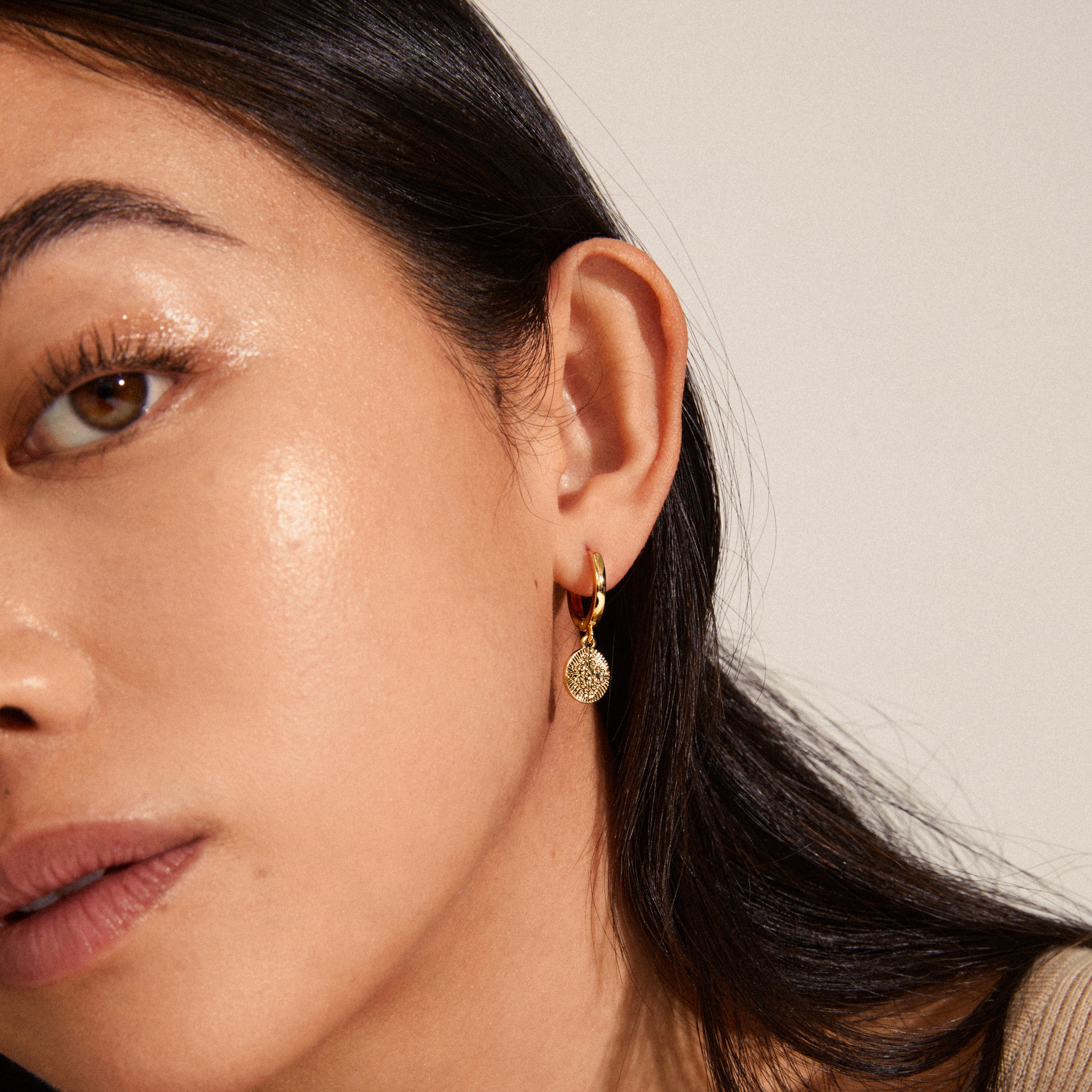 NOMAD coin huggie hoop earrings, gold-plated, worn by a woman with dark hair; features delicate hoop design and coin pendants, showcasing elegance and style.