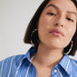 FORCE mega hoop earrings in white and gold-plated, worn by a woman with short dark hair, complementing her blue striped shirt and casual summer style.