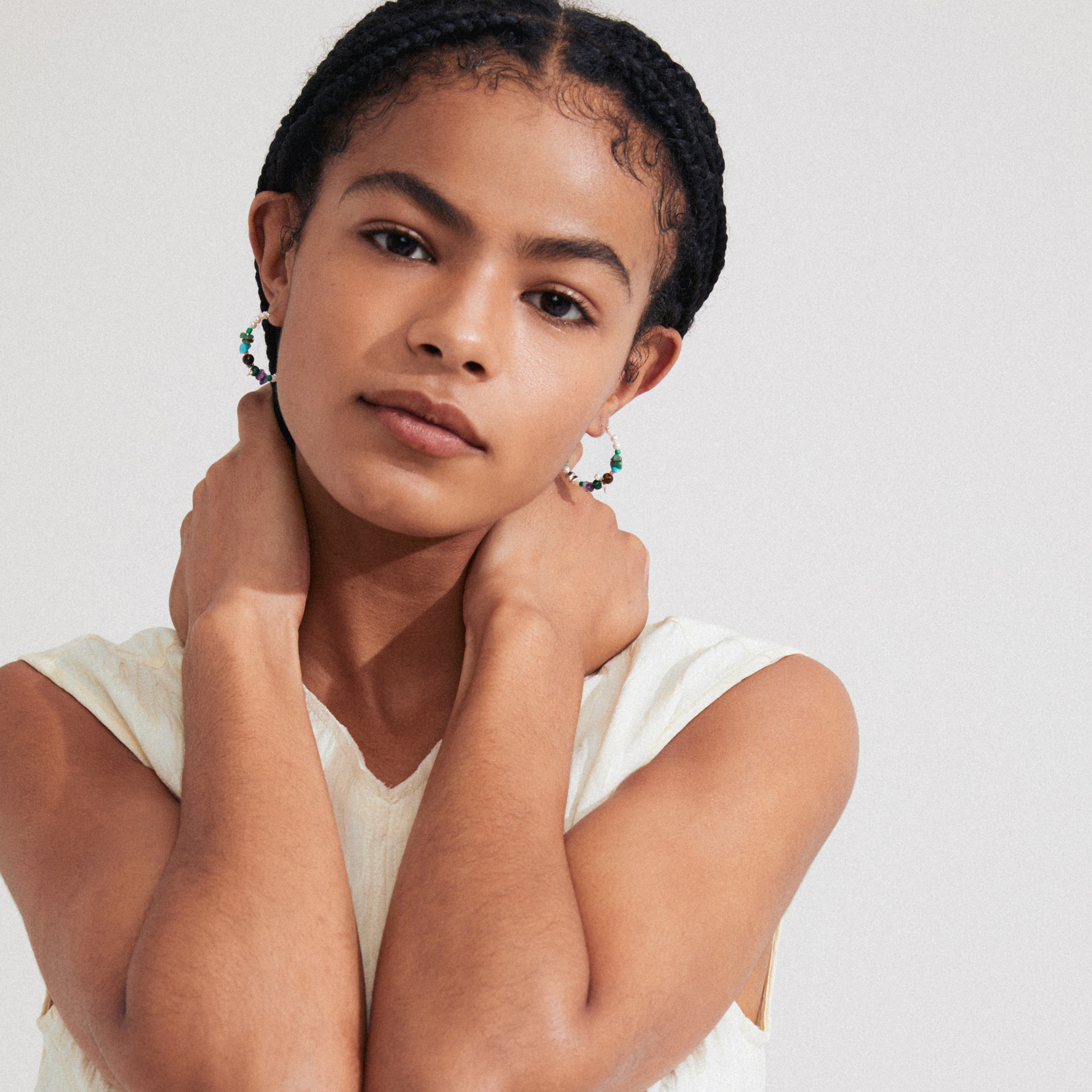 A woman with braids holds her neck, showcasing FORCE hoop earrings multi/silver-plated from Pilgrim, highlighting boho luxe and beachy vibes.