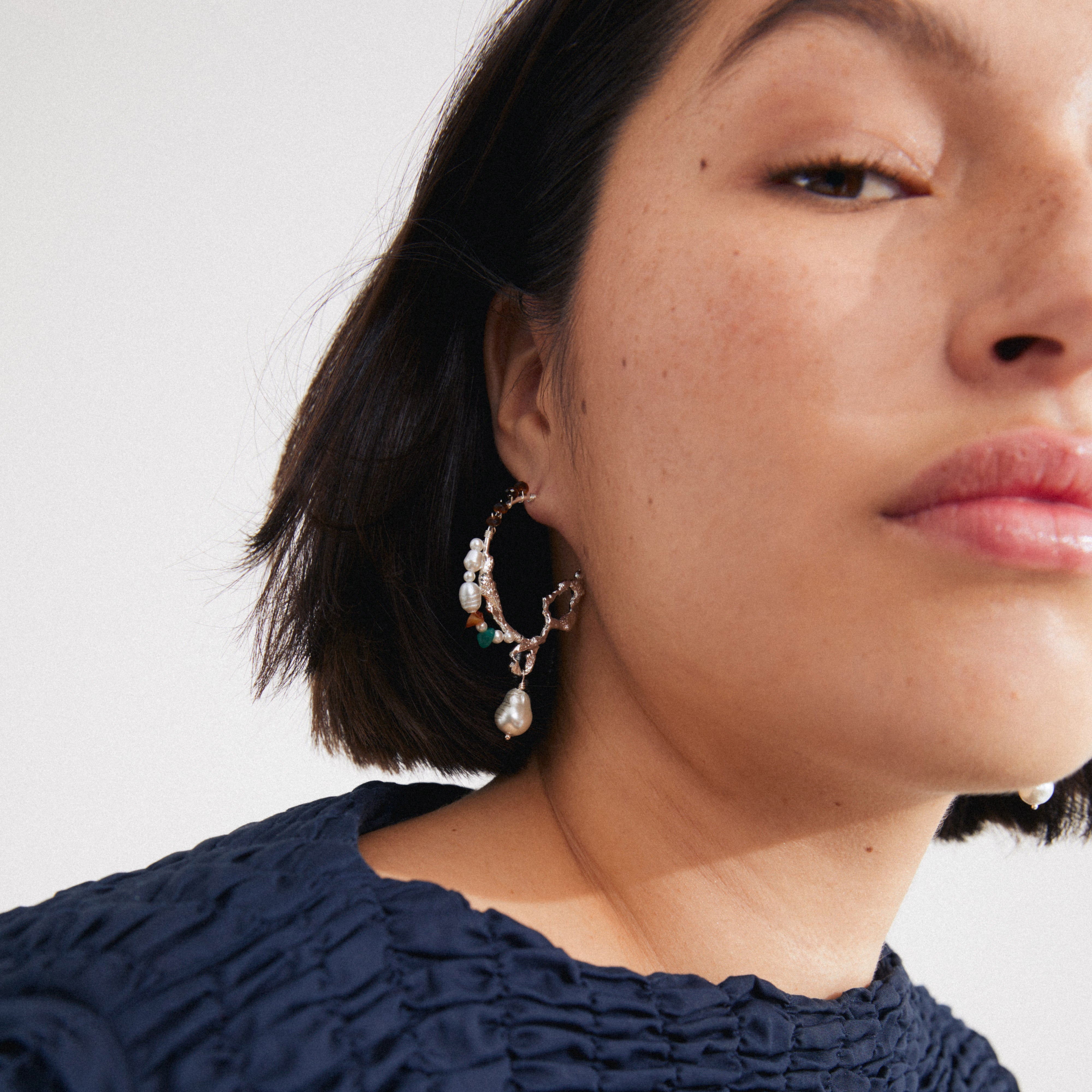 Woman wearing Pilgrim's FORCE large hoop earrings, featuring freshwater pearls and semi-precious gemstones, silver-plated with a bohemian design. Close-up highlights elegant craftsmanship.