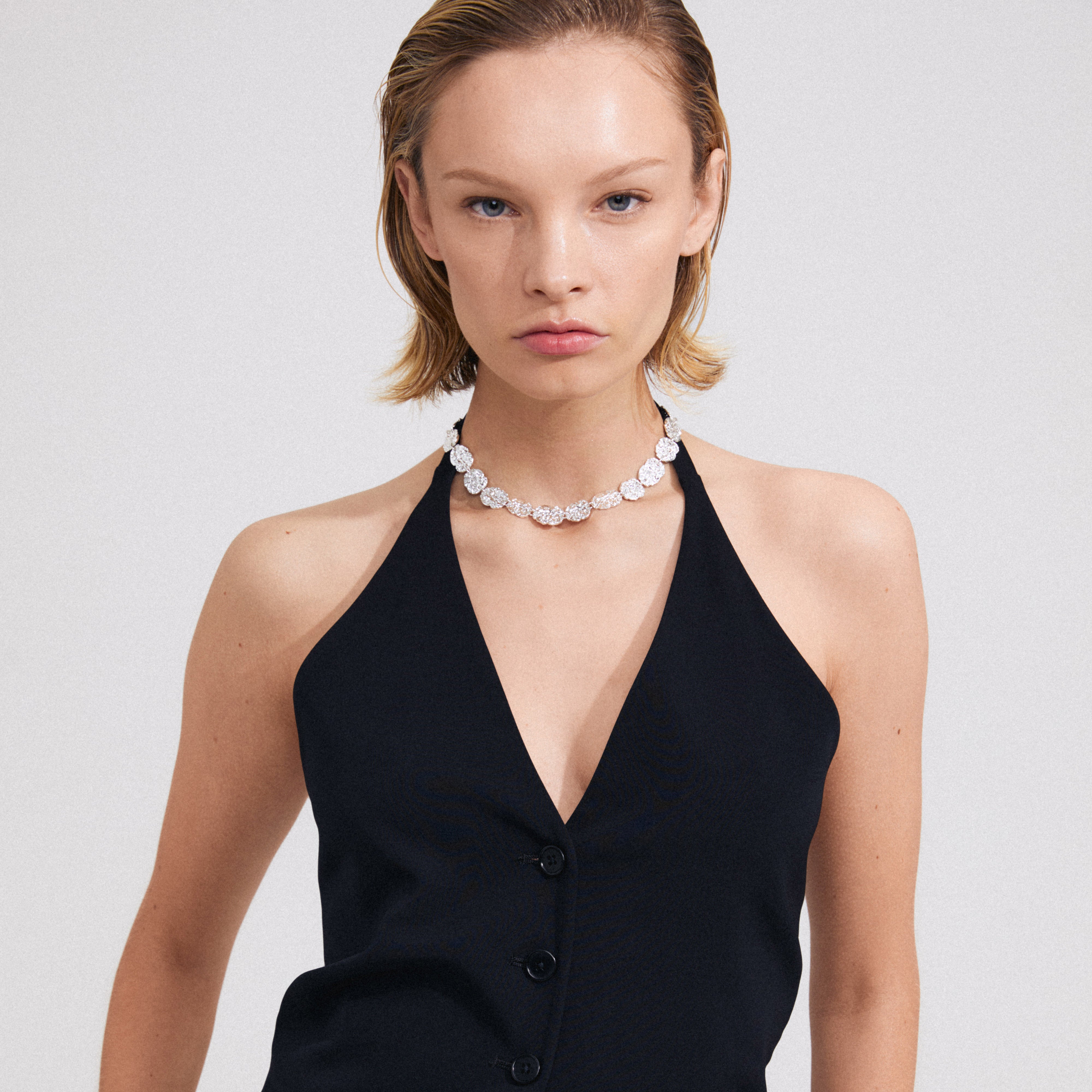 Close-up of a woman wearing Pilgrim's TRUE necklace, showcasing silver-plated, textured coins that lift her stylish black dress ensemble.