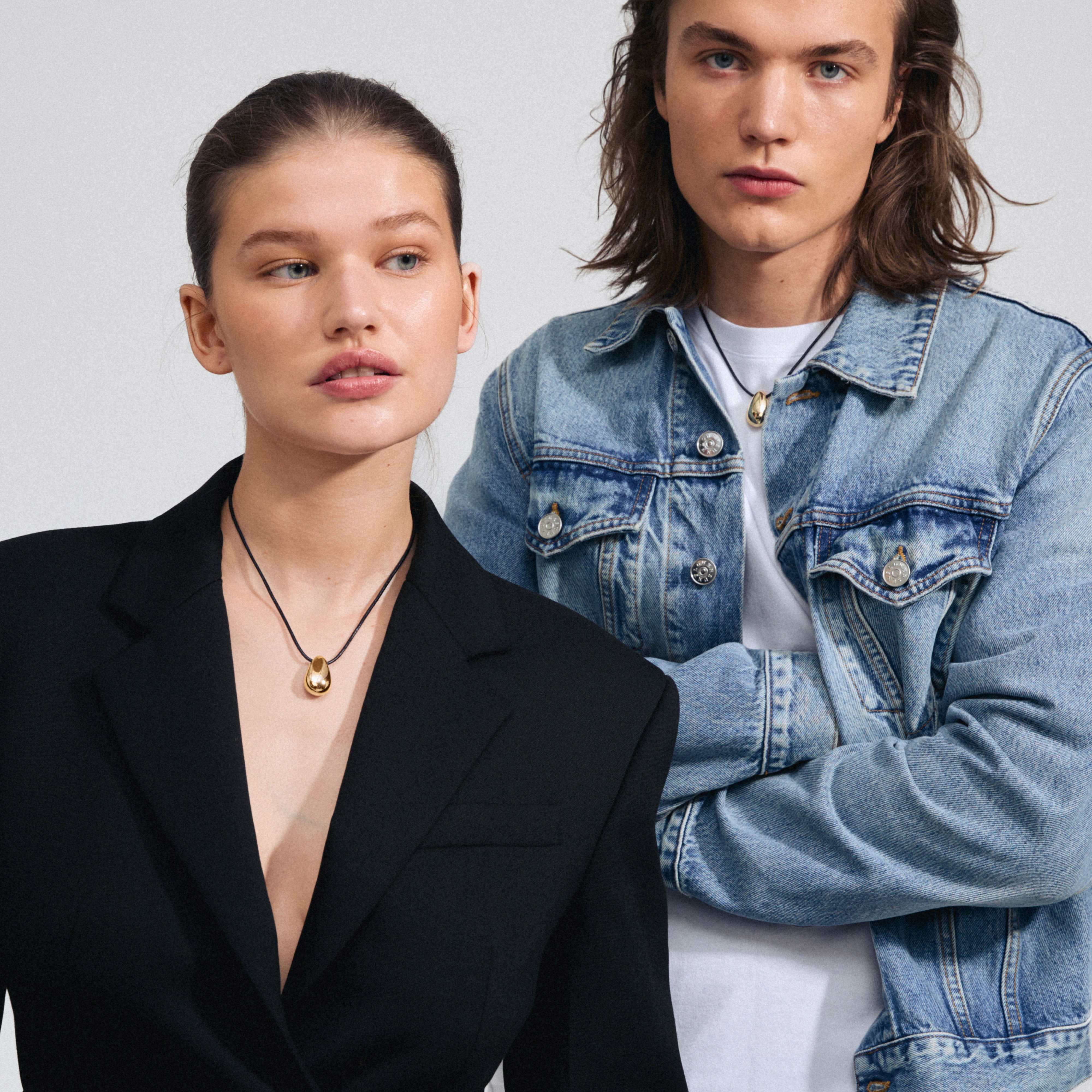 INTENT necklace gold-plated on a man and woman, featuring a black leather cord and teardrop pendant, embodying Scandinavian style and sustainability from Pilgrim.