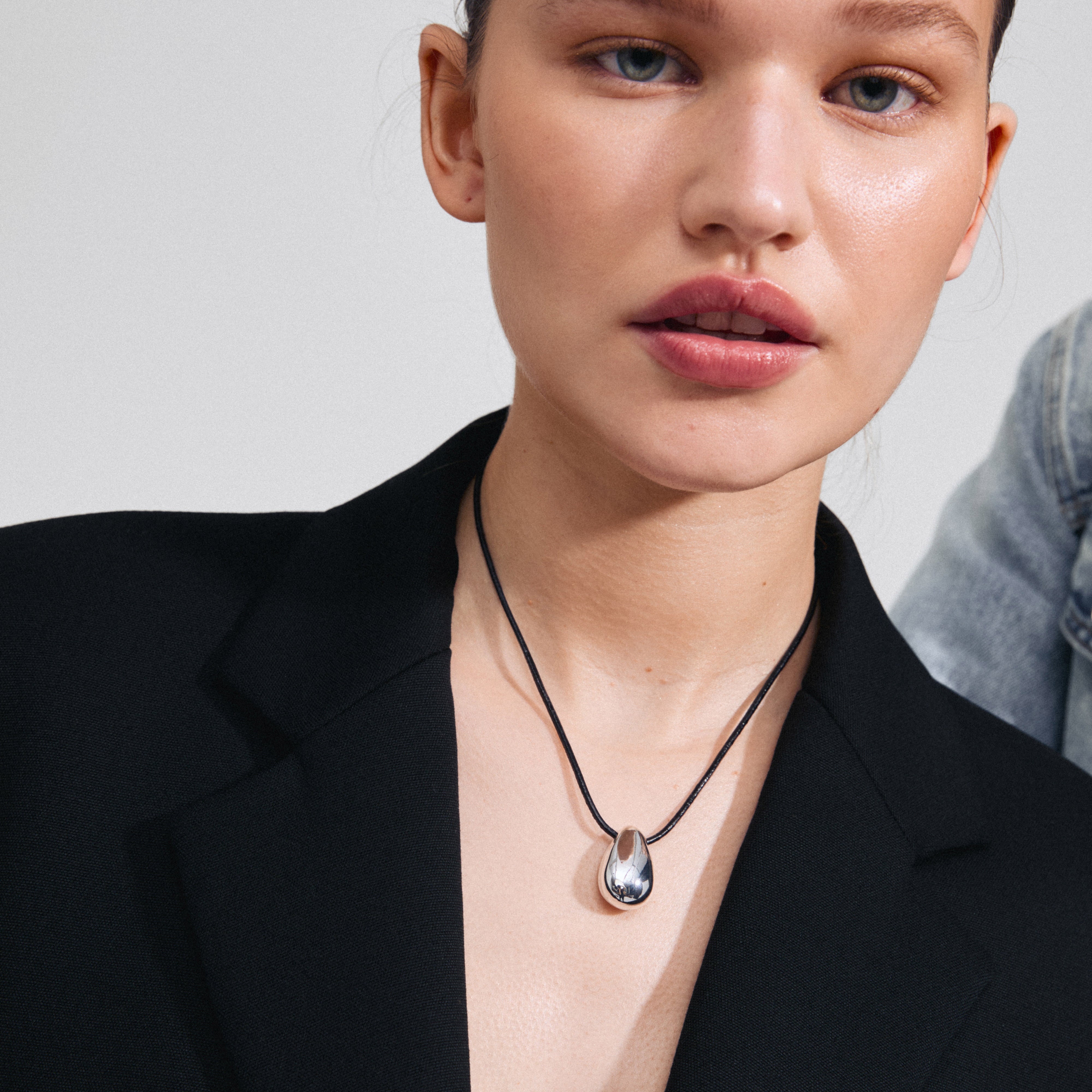 INTENT necklace silver-plated featuring a teardrop pendant on a black leather cord, worn by a woman, highlighting Scandinavian design and recycled materials.