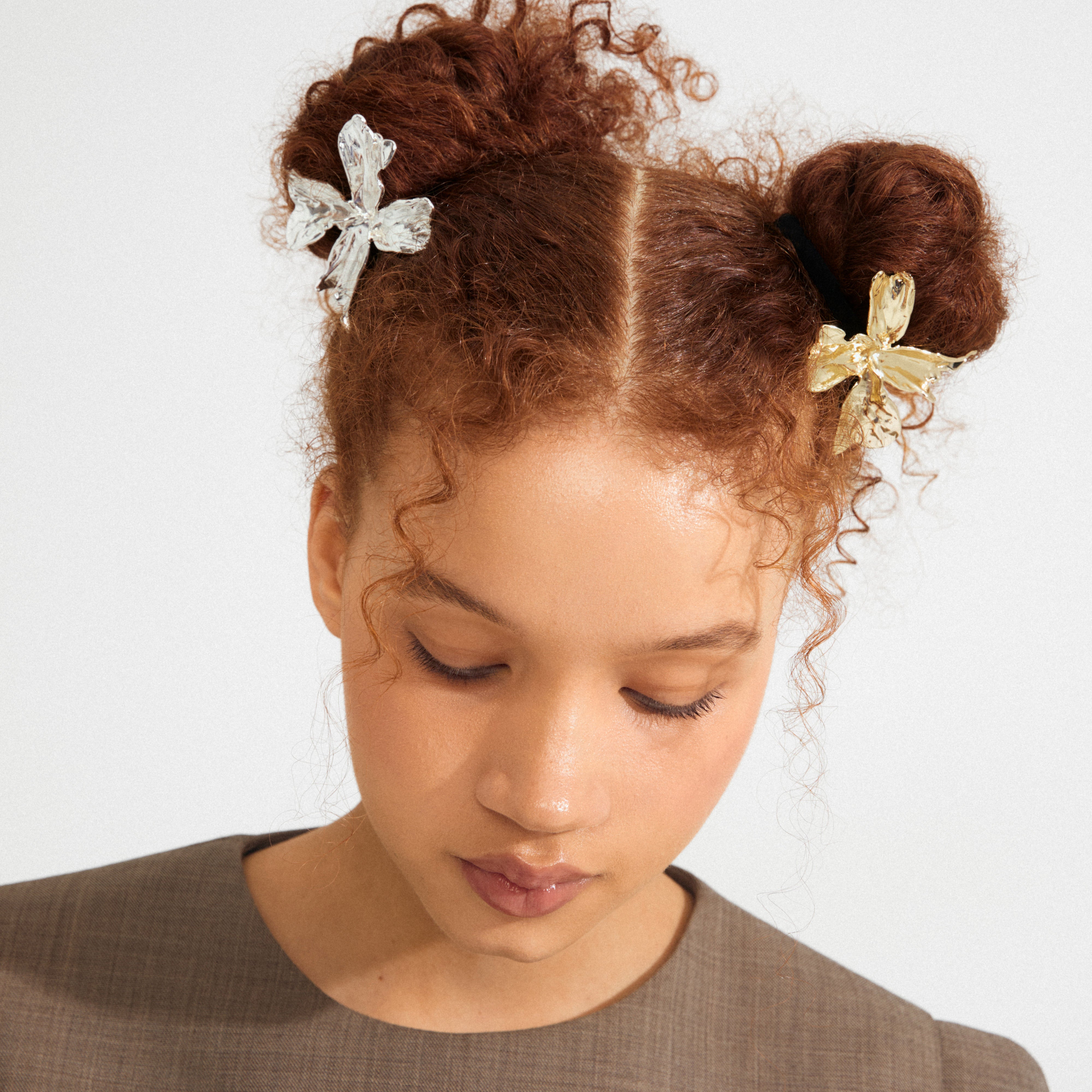 Young person with curly hair styled in space buns, adorned with Pilgrim's DREAM gold-plated flower hair accessory, adding an elegant touch to their look.