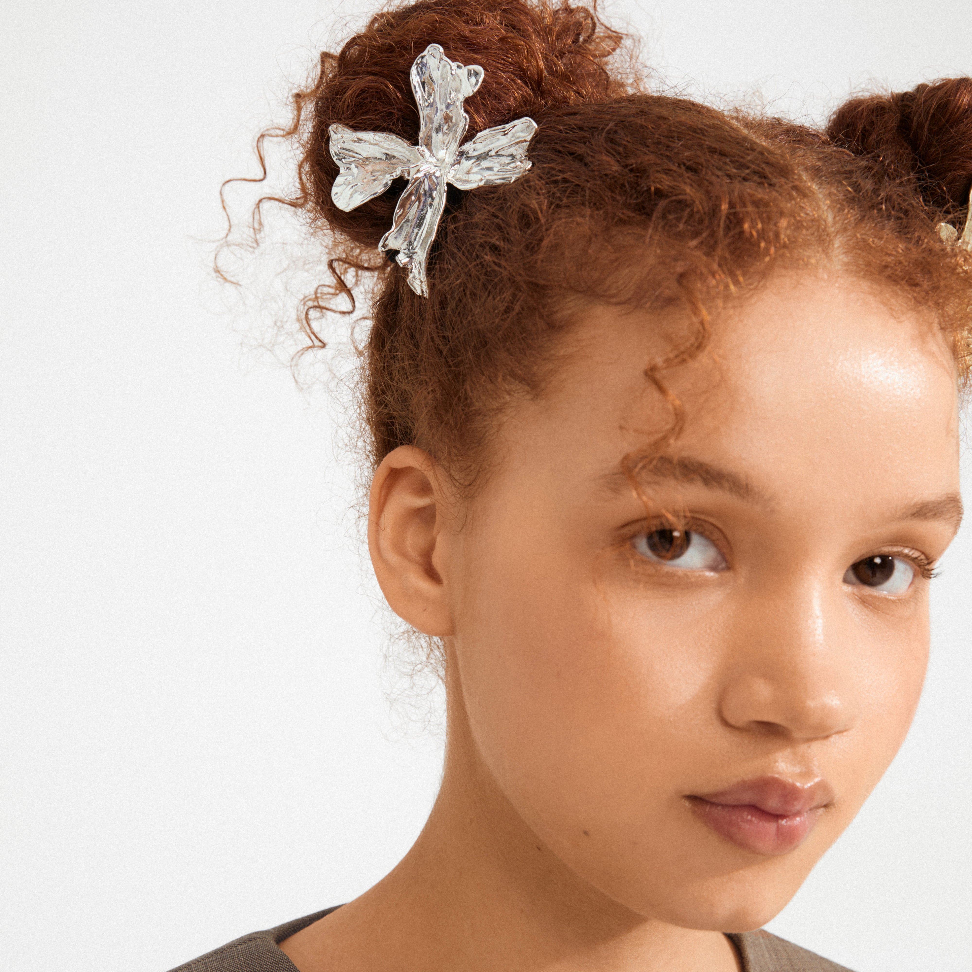 Young person with curly buns wearing the DREAM hair-accessory silver-plated, featuring a four-petaled flower clip, embodying Pilgrim's eco-conscious, stylish design.
