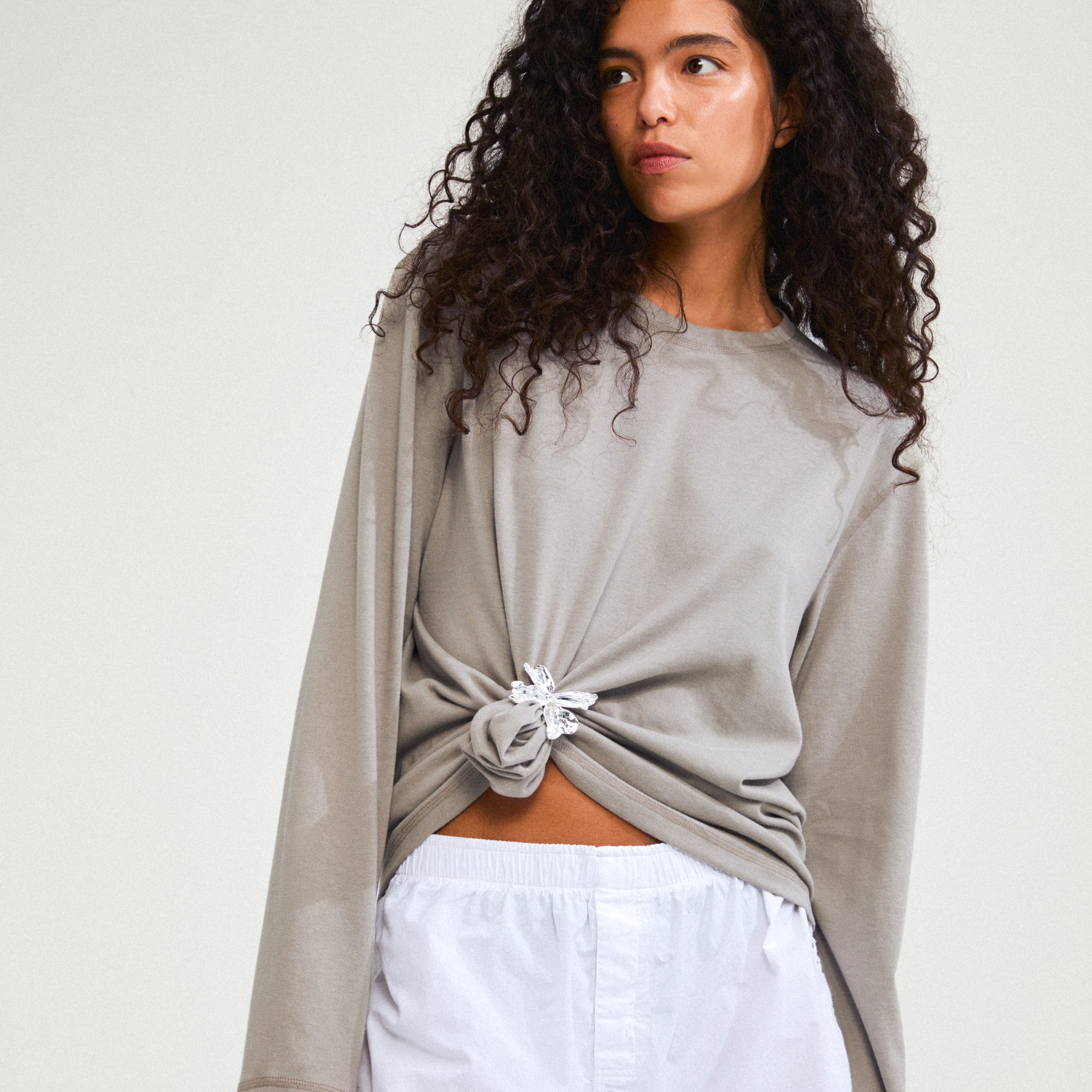 Woman wearing taupe shirt with a DREAM hair-accessory silver-plated, featuring a large flower charm, styled in her hair, adding elegance to her look.