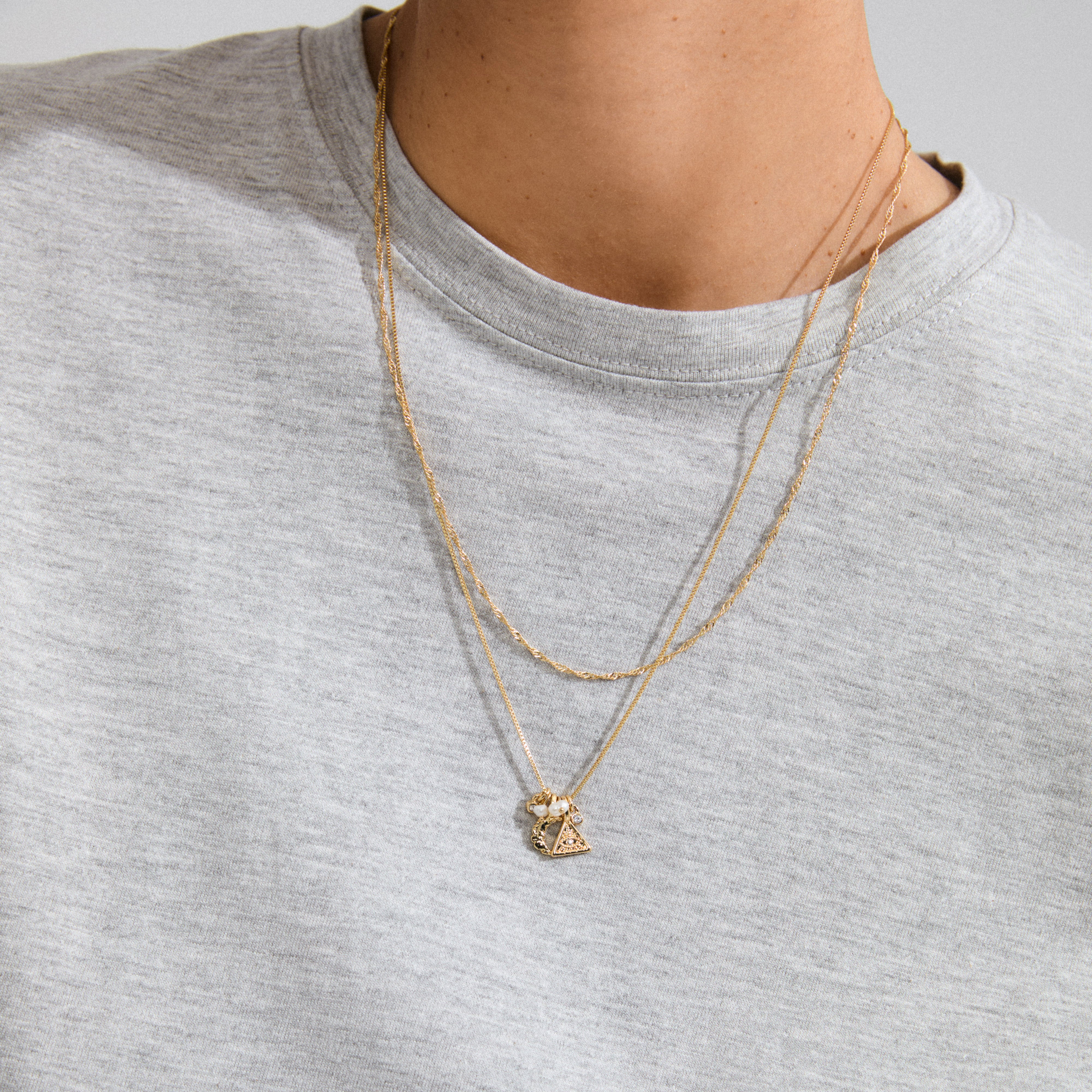 BETWEEN necklace 2-in-1 gold-plated features sleek box and twisted chains with pendants like an all-seeing eye, moon, pearls, and crystals for a boho look.