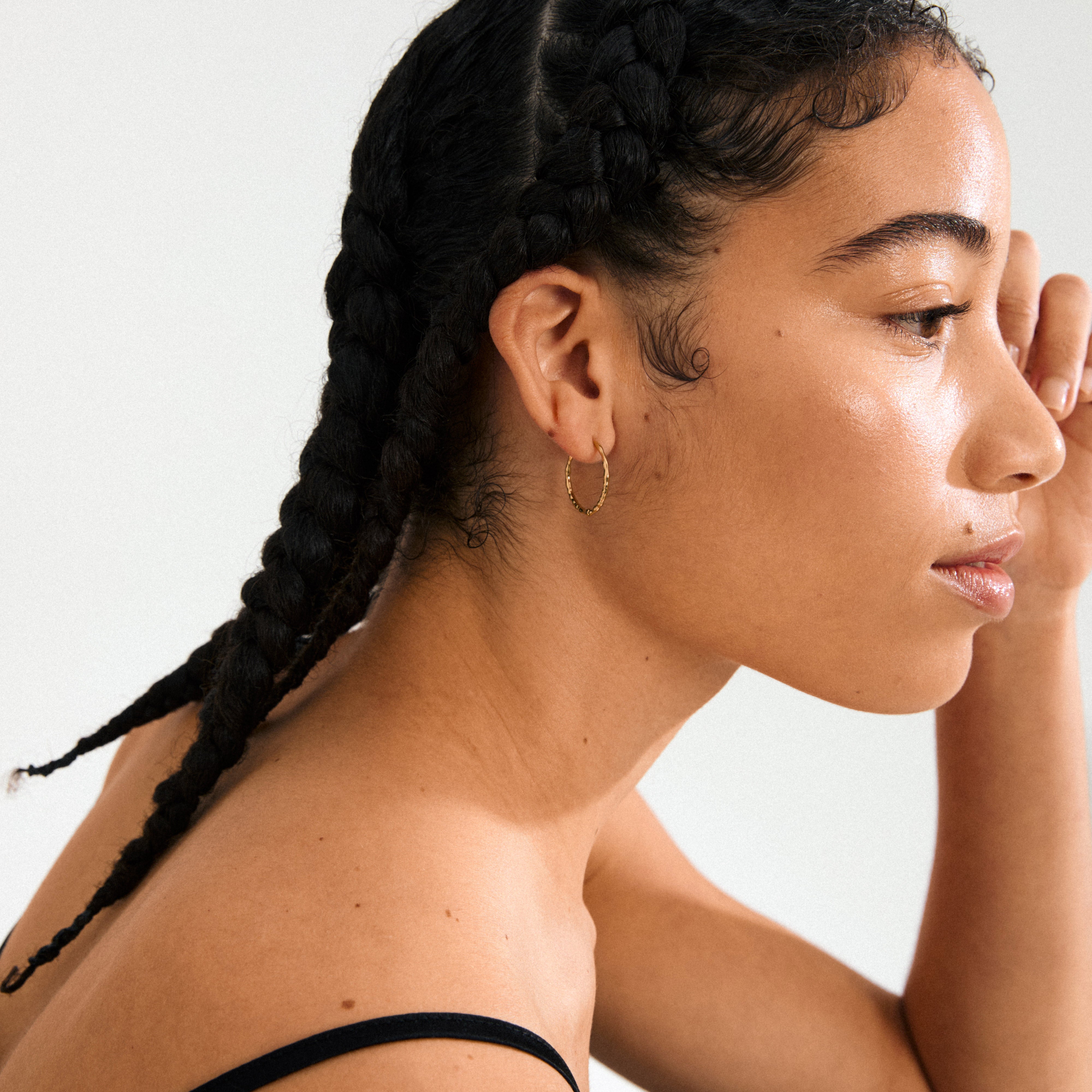 Close-up of BETWEEN hoops gold-plated, showcasing their organic, flowing design and slender silhouette, embodying minimalist boho style crafted from 99% recycled material.