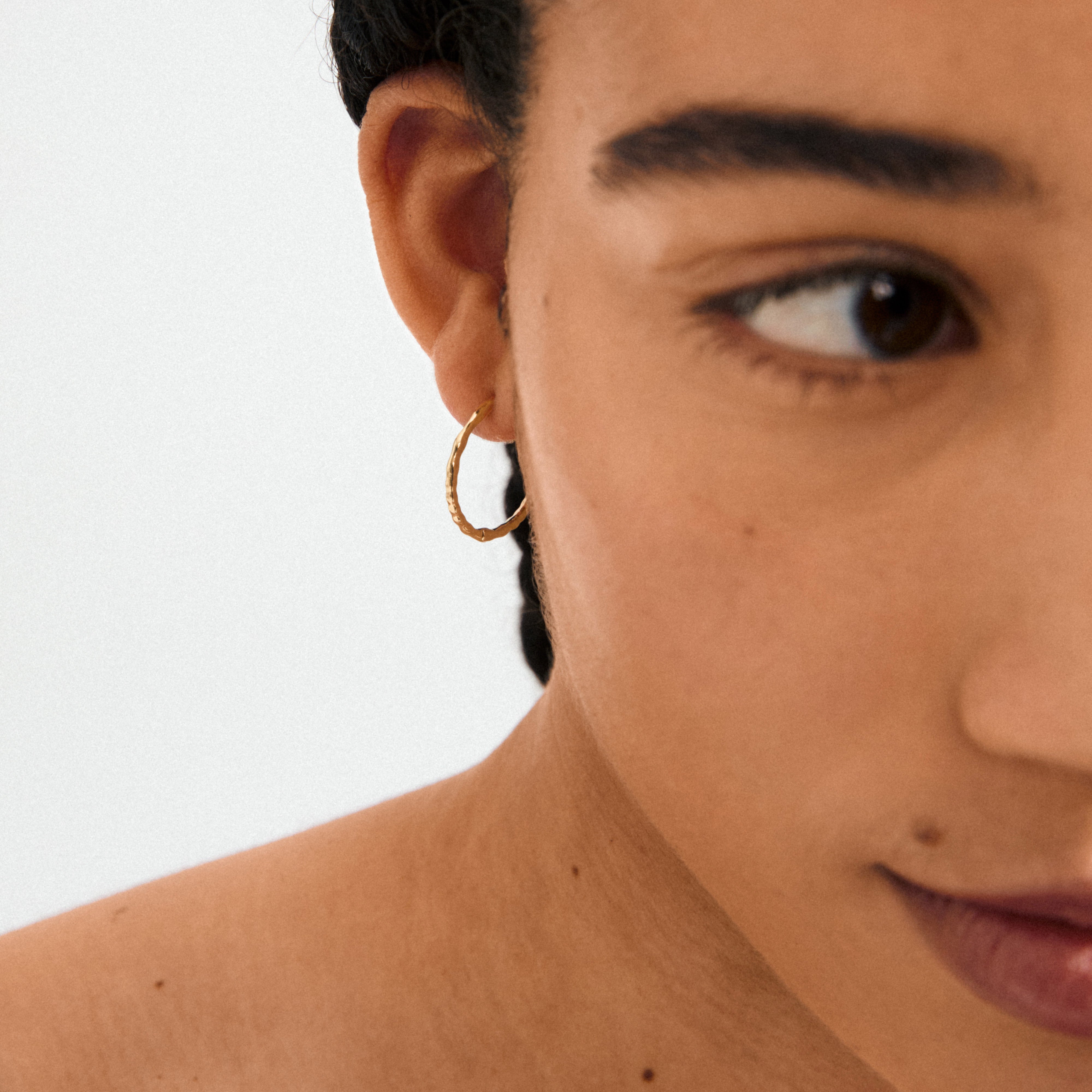 Close-up of a woman's face wearing BETWEEN hoops, gold-plated with an organic design, showcasing minimalist, boho-inspired style crafted from recycled material.