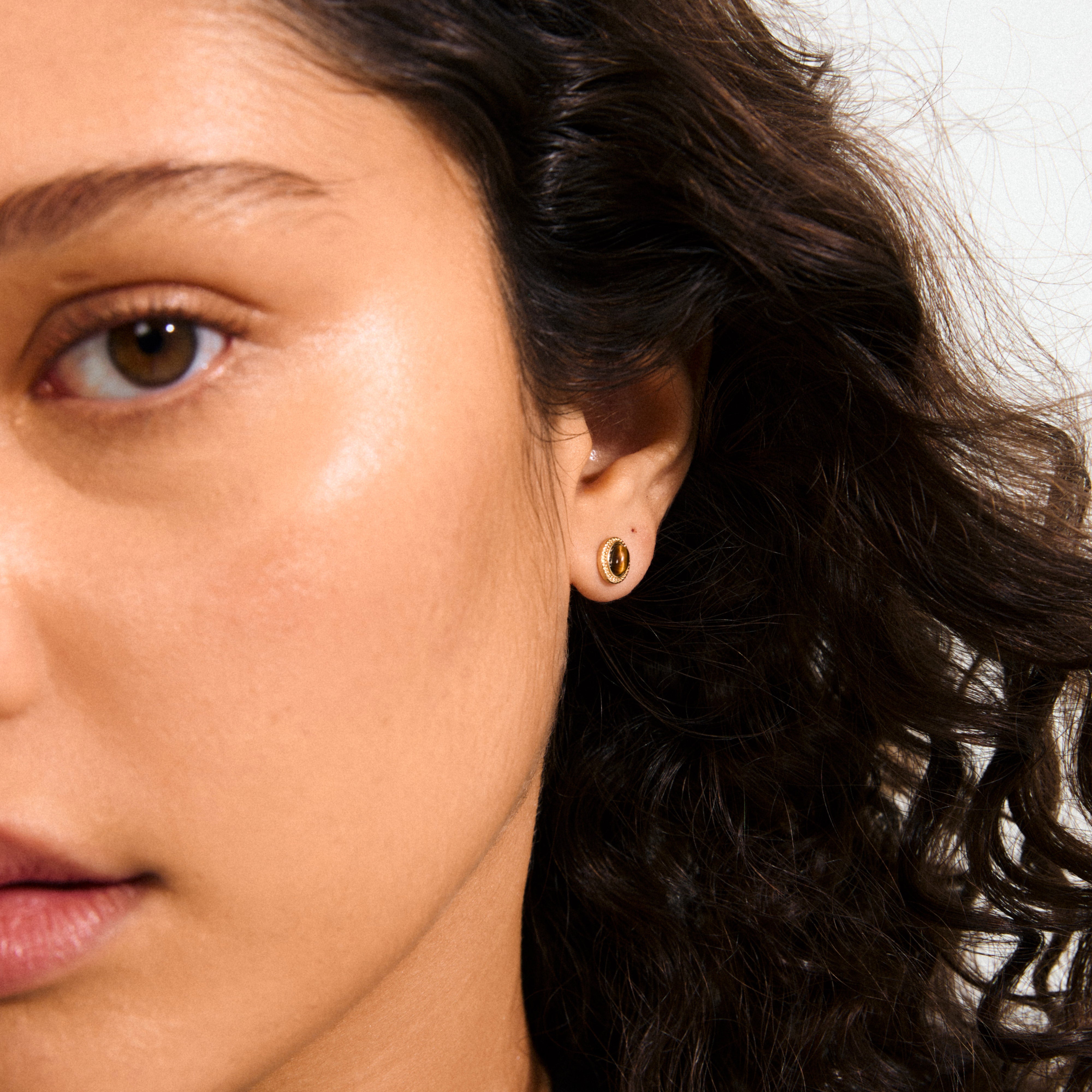 Close-up of a woman's face showcasing Pilgrim's BETWEEN gold-plated stud earrings with cabochon-cut Tiger Eye stones, exuding boho chic and vintage elegance.