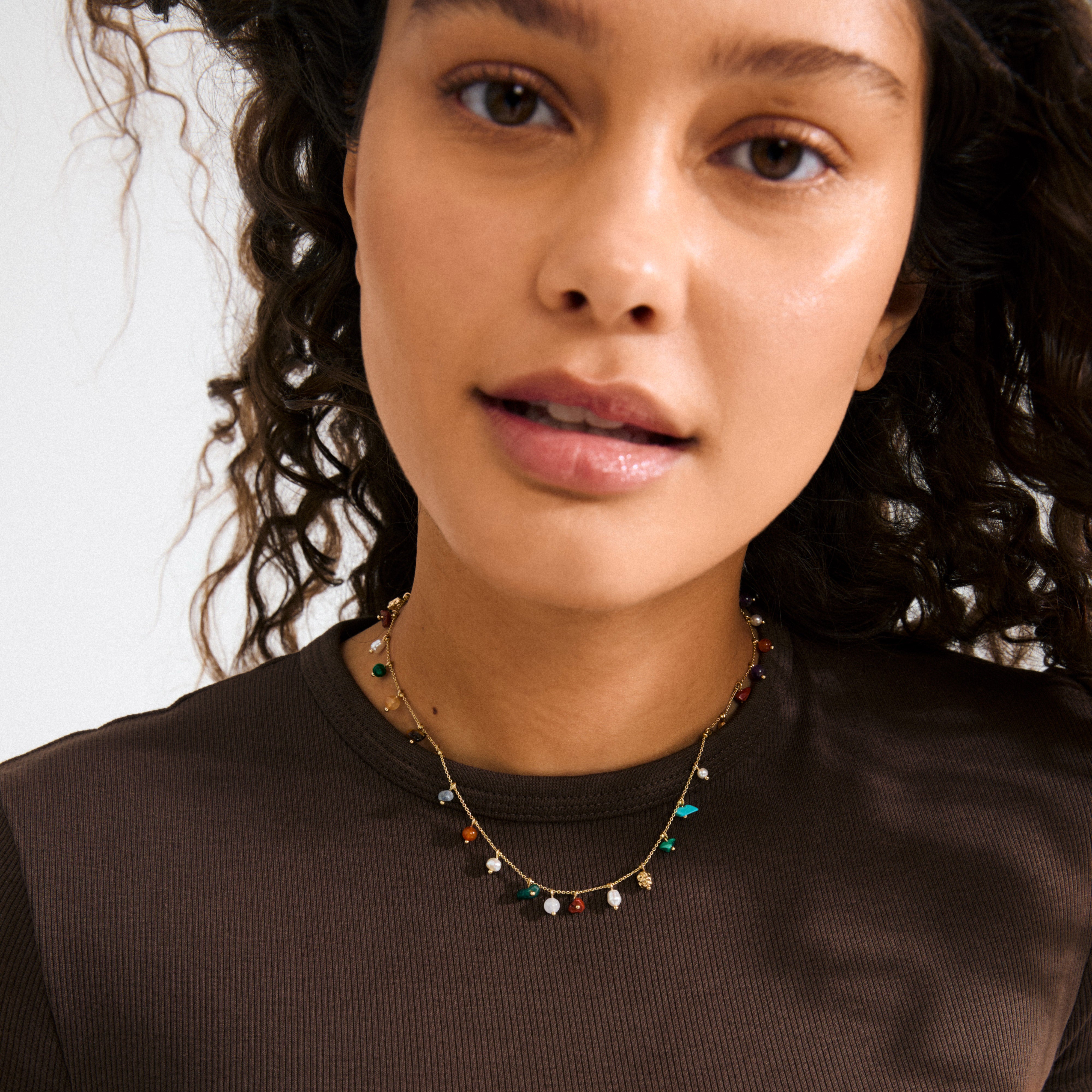 Close-up of a woman's face wearing Pilgrim's gold-plated BETWEEN necklace with vibrant semi-precious stones, showcasing luxe boho style.