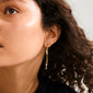 Close-up of a woman's ear wearing Pilgrim's BETWEEN gold-plated chain earrings with asymmetrical design and vibrant pendants, showcasing a bohemian and artistic style.