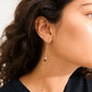 Close-up of a woman's ear showcasing Pilgrim's BETWEEN gold-plated chain earrings with asymmetrical hoops and vibrant gemstone pendants, exuding a bohemian elegance.