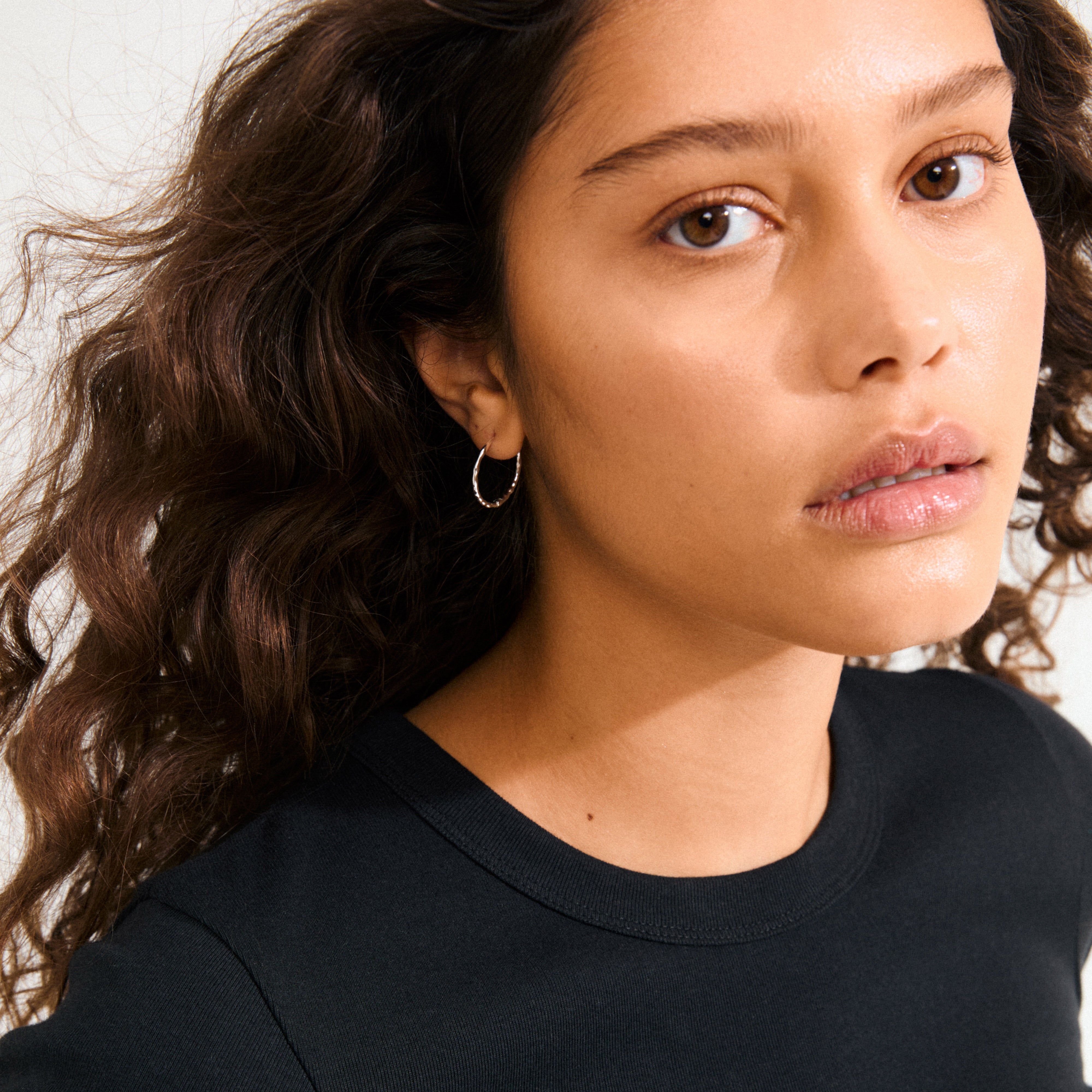 Silver-plated BETWEEN hoops with an organic, flowing design, shown close-up. These minimalist earrings offer a boho twist, perfect for versatile styling.